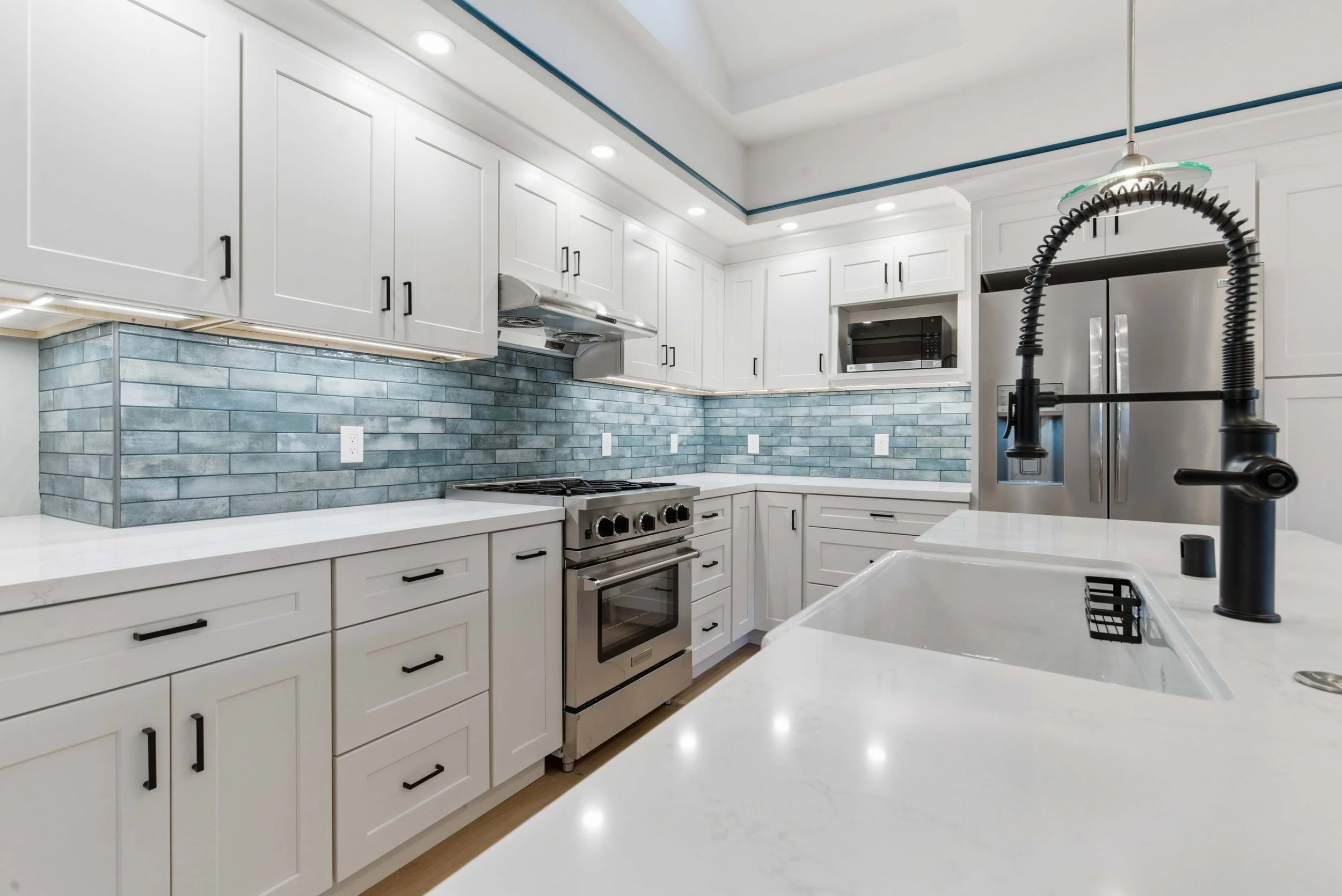 White cabinets with blue tiles, a marble countertop and sink are in the foreground.