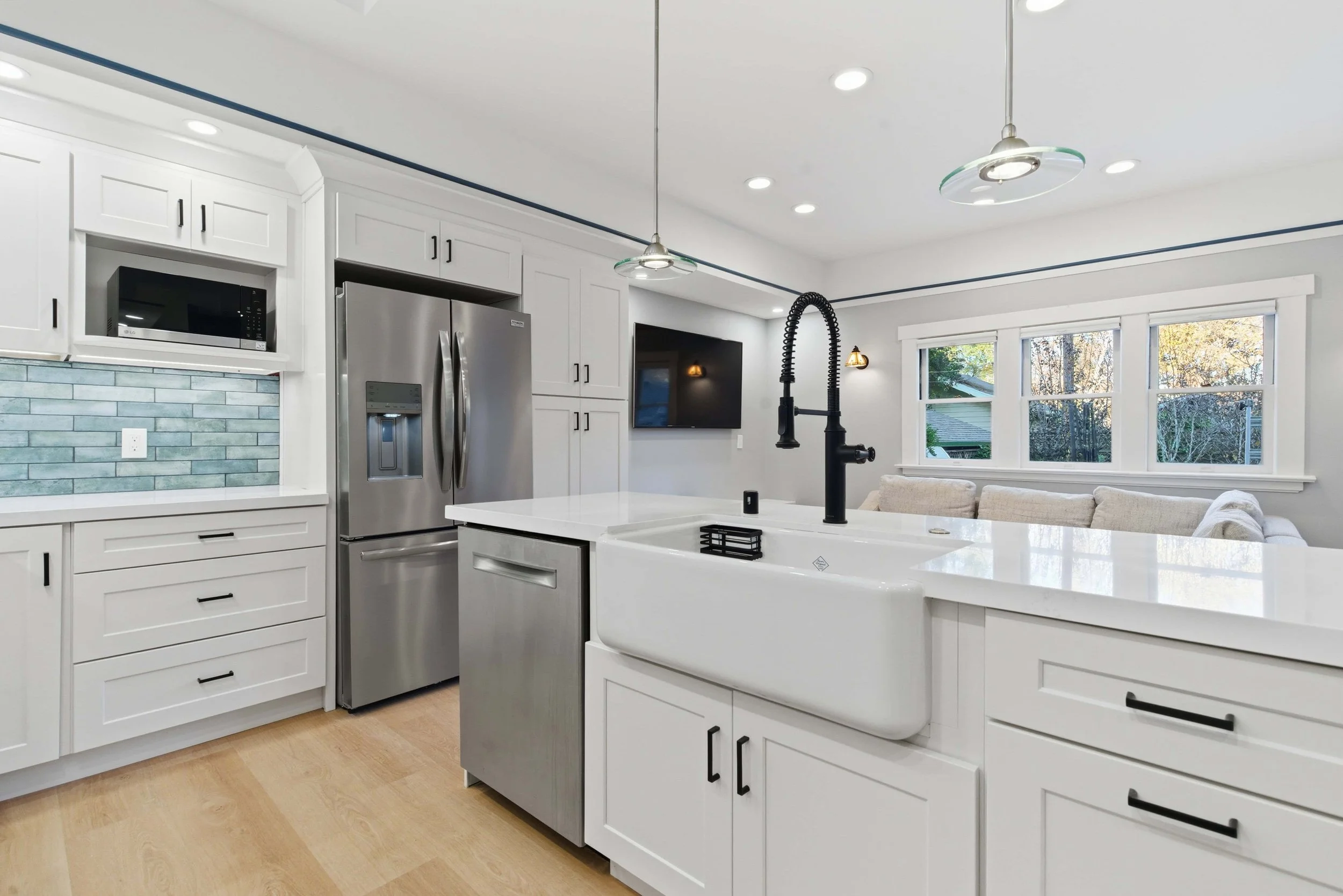 Naglee Park kitchen remodel, white cabinets, wood floors, stainless appliances, apron sink, and matte black commercial style faucet. Two glass pendant lamps overhang the sink area.