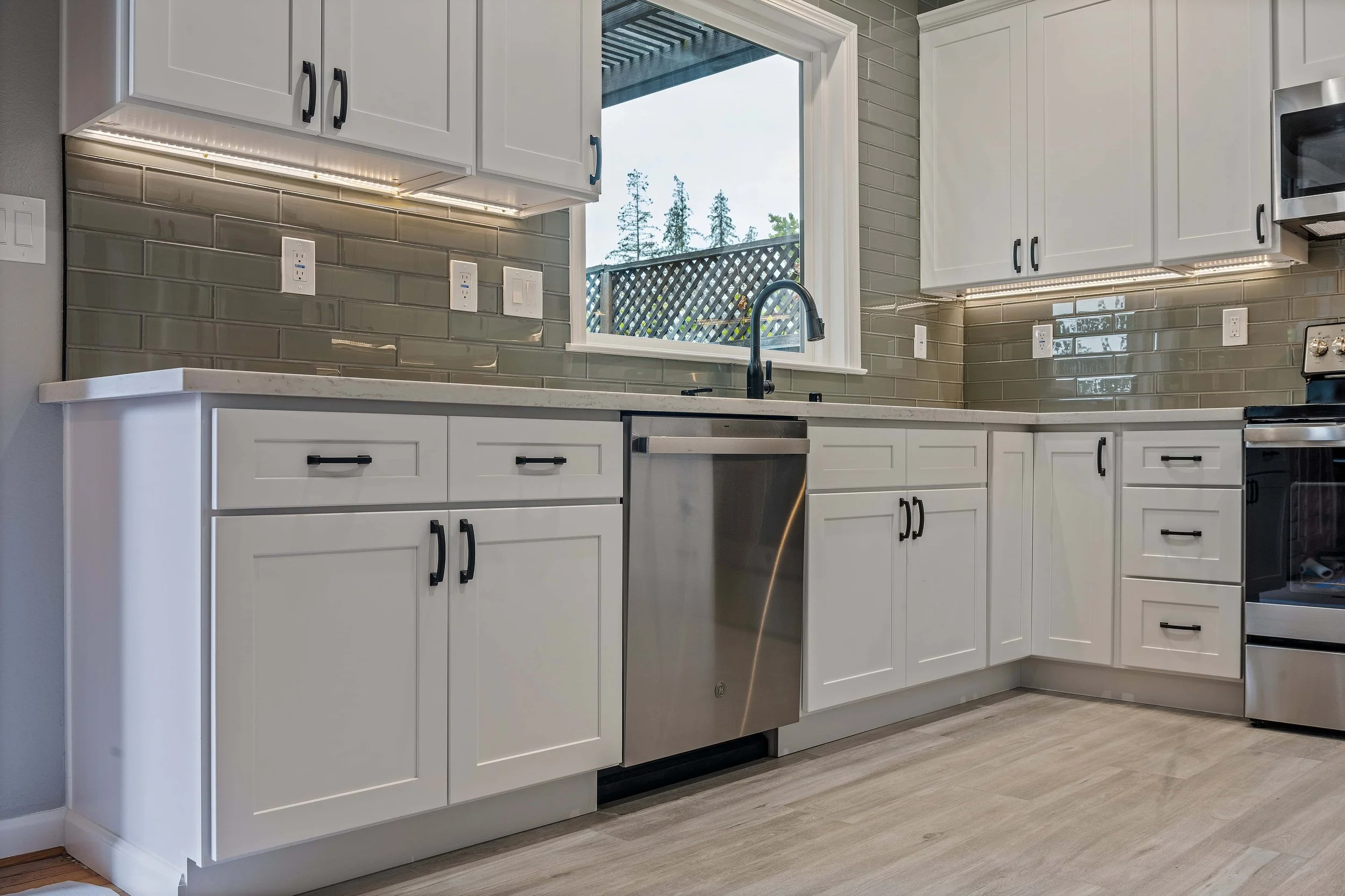 White kitchen cabinets with black handles. The floor, white planks, is also visible.