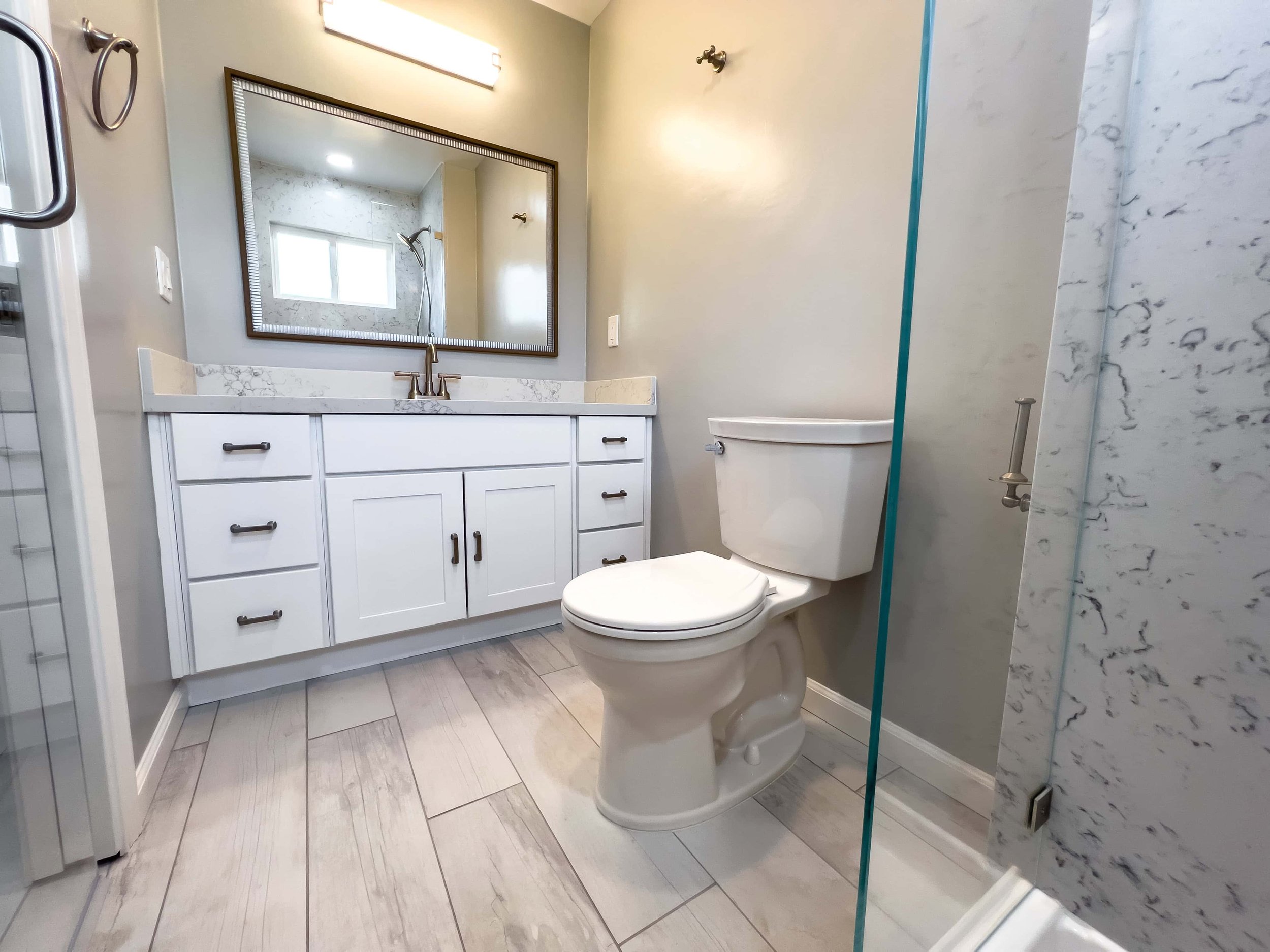 A renovated California bathroom with bright, light walls, marble, and bright white plank flooring