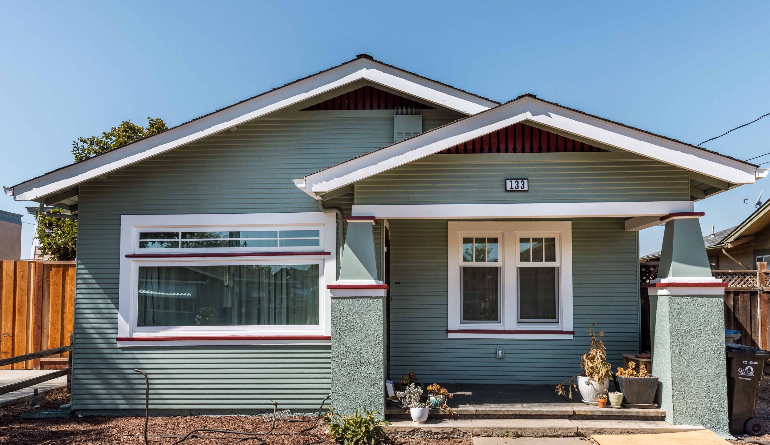 Downtown San Jose cottage with sage/blue paint and red highlights. The house has horizontal siding and white trim.