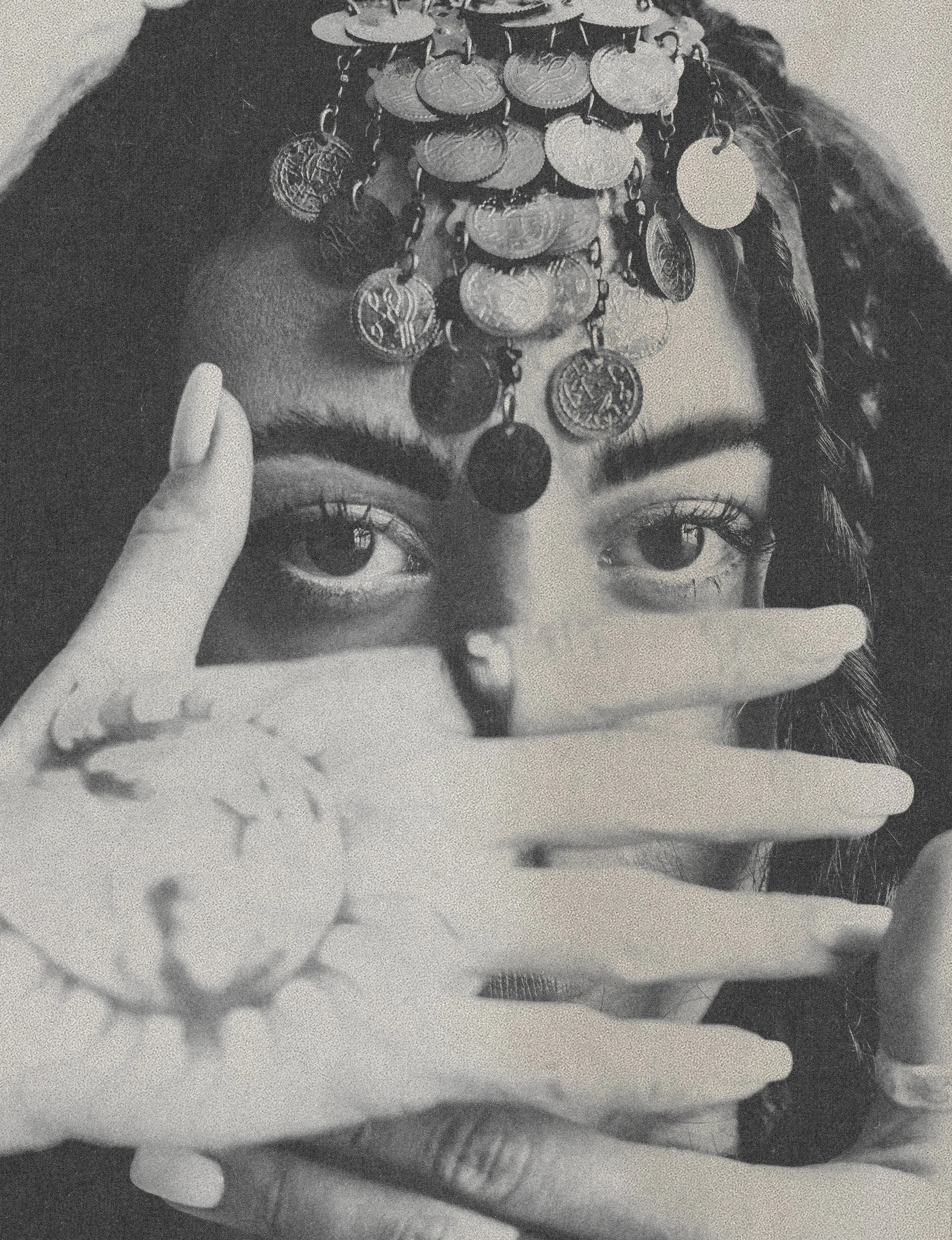 A person with braided hair is holding a photograph up to their face. The photograph shows a woman's face decorated with multiple layers of coins on her forehead, eyes, and chin. The person's finger is pointing to the woman's lips in the photograph.