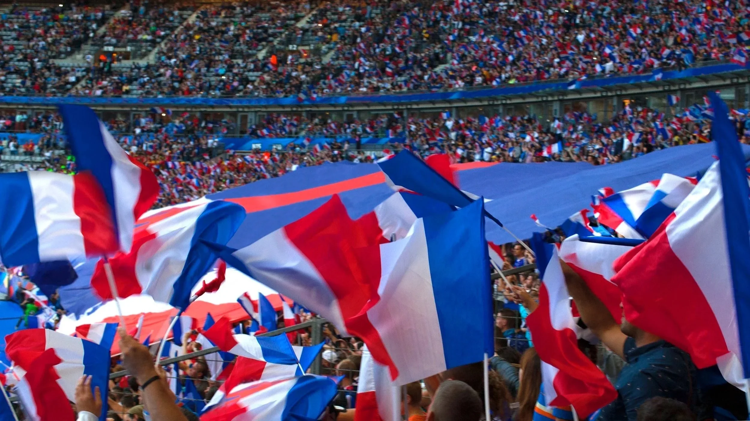 Crowd at a stadium waving red, white, and blue flags.