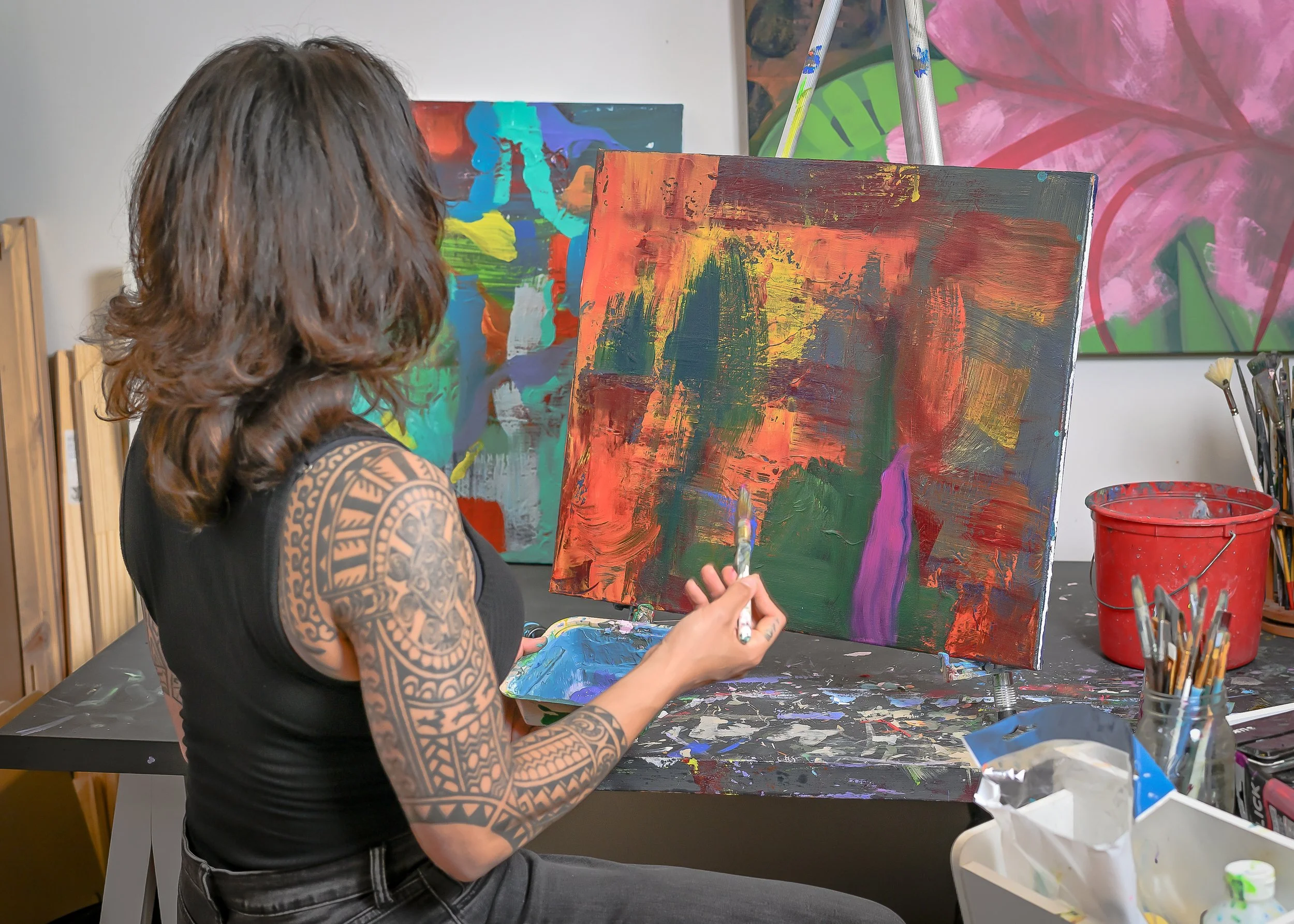 Samantha Juan painting a vibrant abstract artwork in her studio, surrounded by colorful canvases and art supplies.