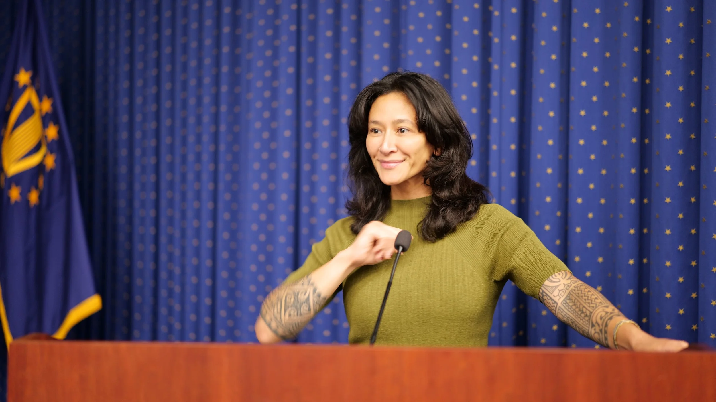 Samantha Juan smiling and speaking into a microphone during a public event.