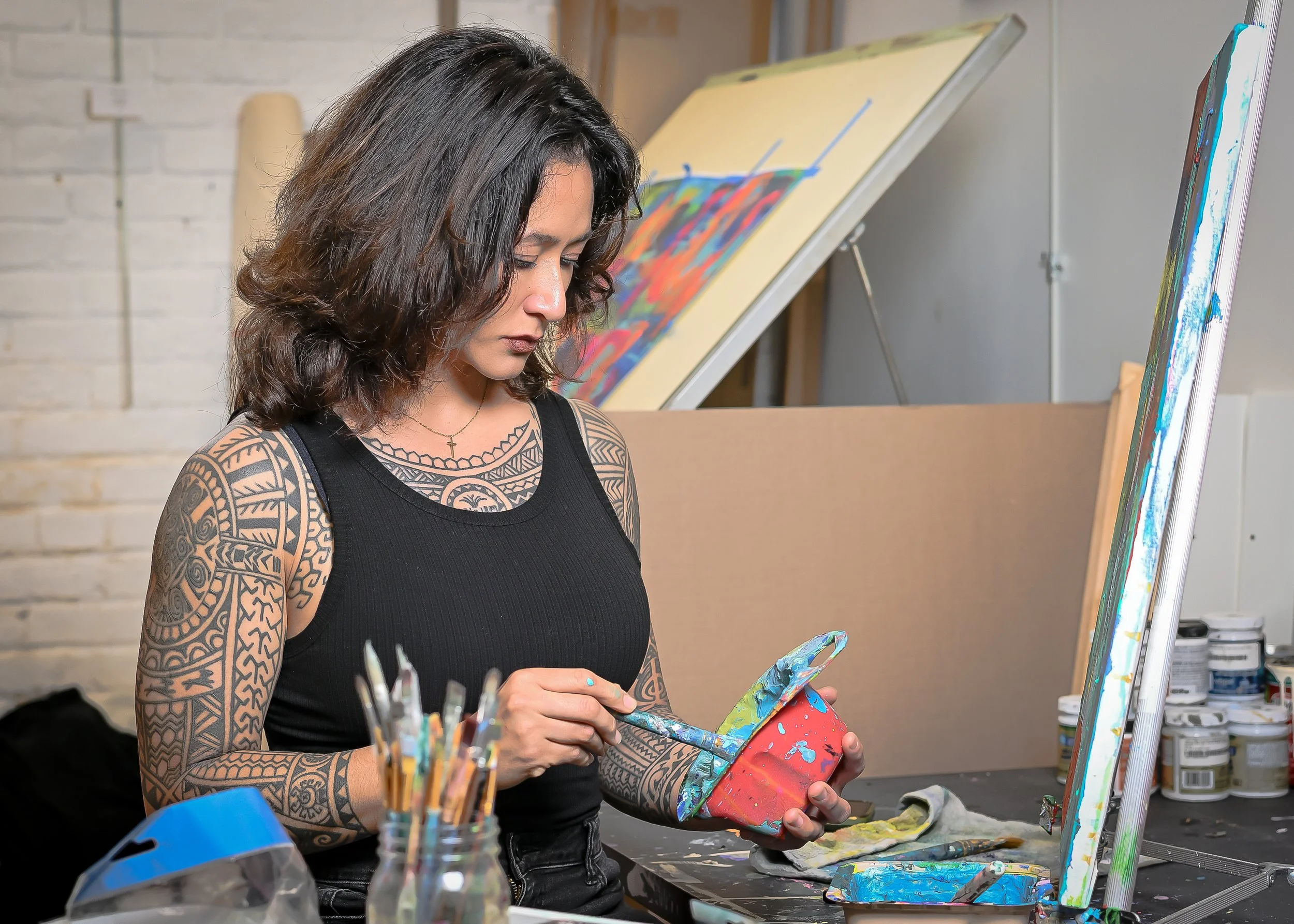 Samantha Juan painting on canvas in her art studio while holding a palette and brush.