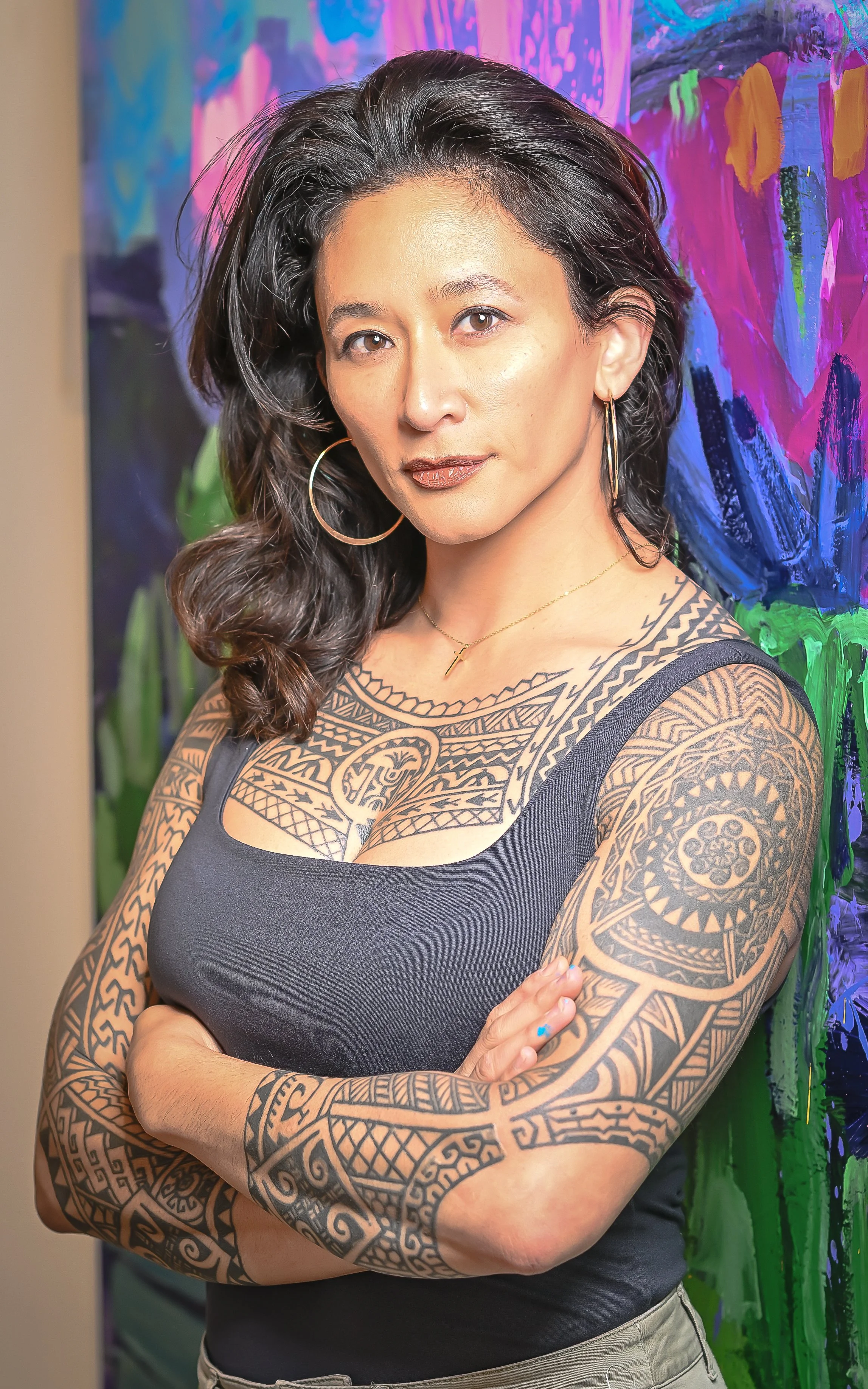 Sam Juan standing with her arms crossed in front of a colorful abstract painting.
