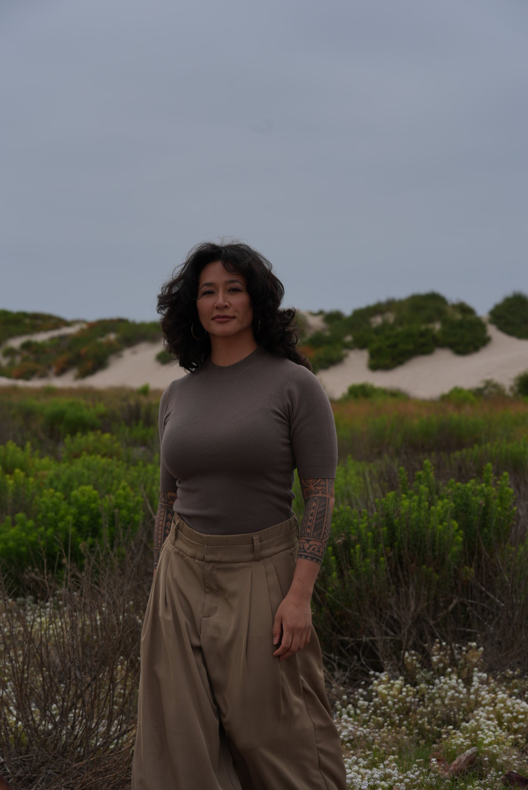 Samantha Juan standing among coastal greenery and sand dunes beneath a cloudy sky.