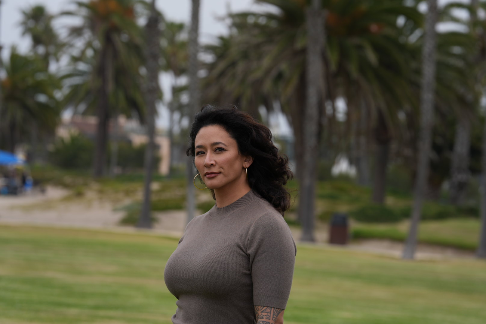 Samantha Juan standing outdoors in a park surrounded by palm trees and greenery.