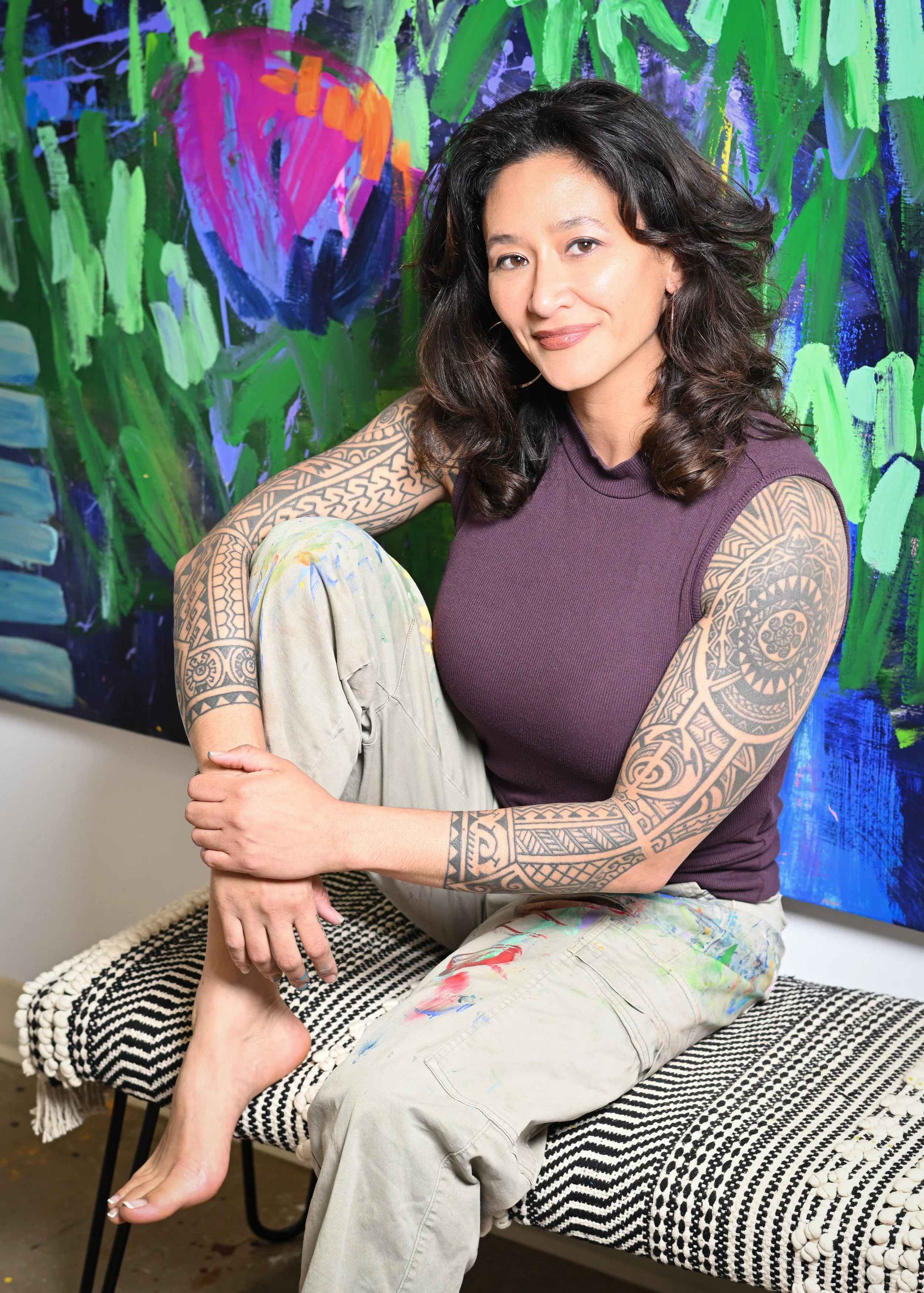 Samantha Juan smiling while seated in front of one of her colorful abstract paintings.