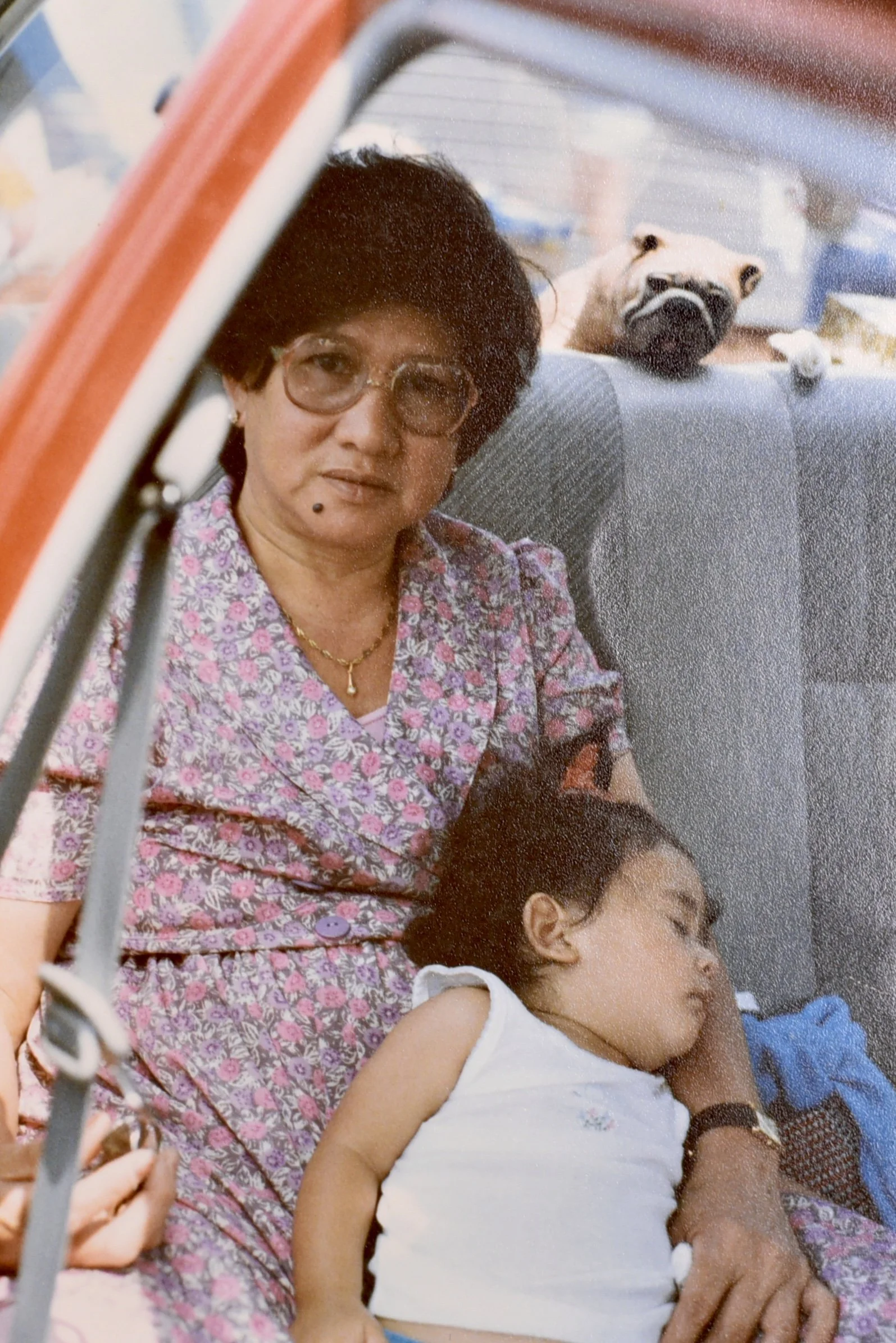 Childhood photograph of Samantha Juan resting on a woman’s lap beside a dog during her early years in Bahrain.