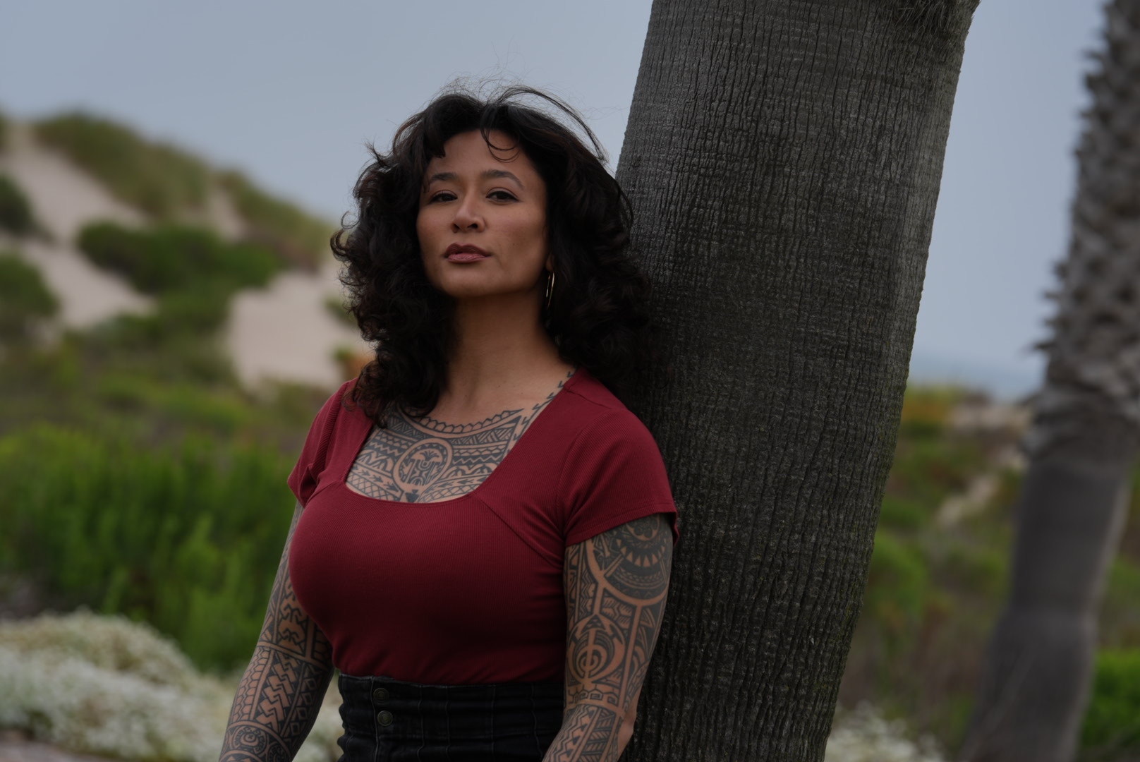 Samantha Juan wearing a red top and leaning against a tree in a natural outdoor setting.