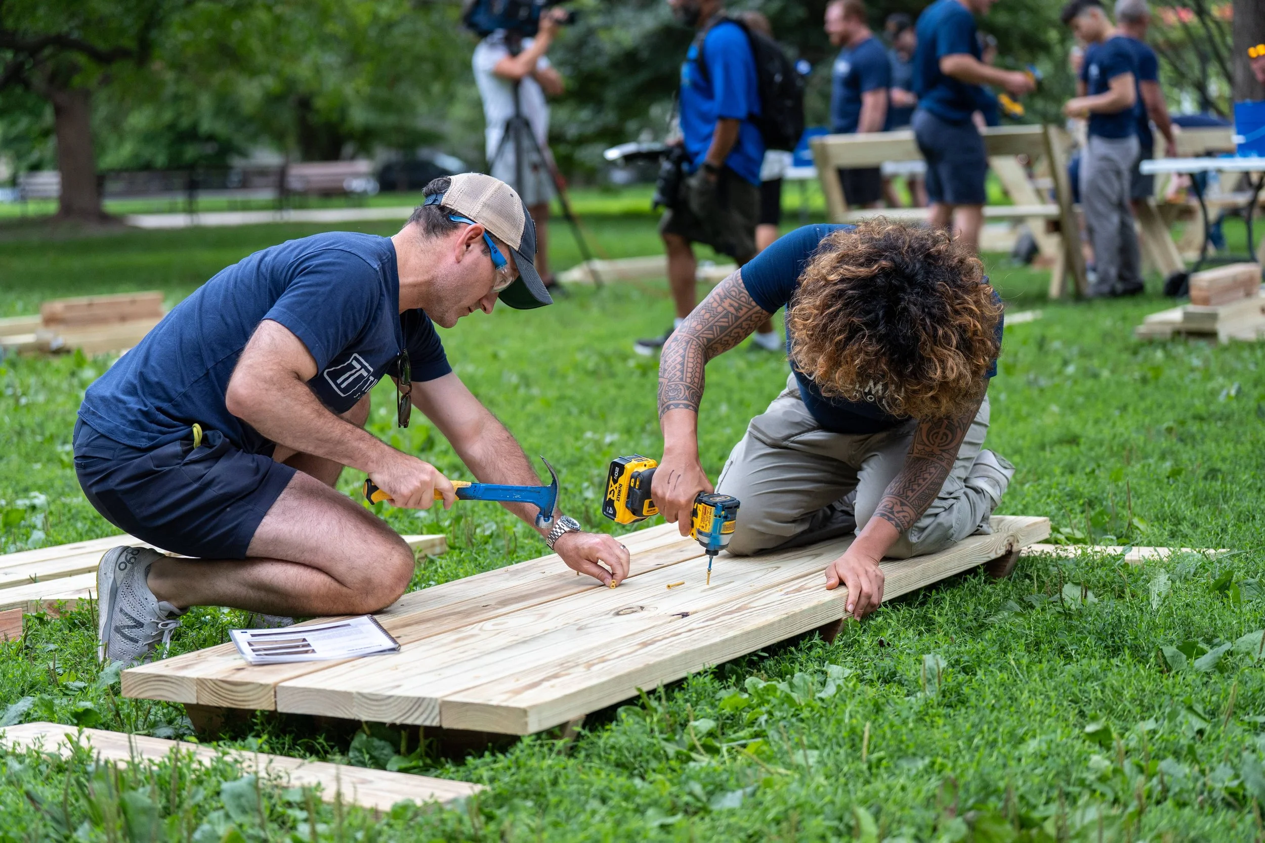 Samantha Juan and another participant kneeling on the grass while assembling a wooden structure during a community event in the park.