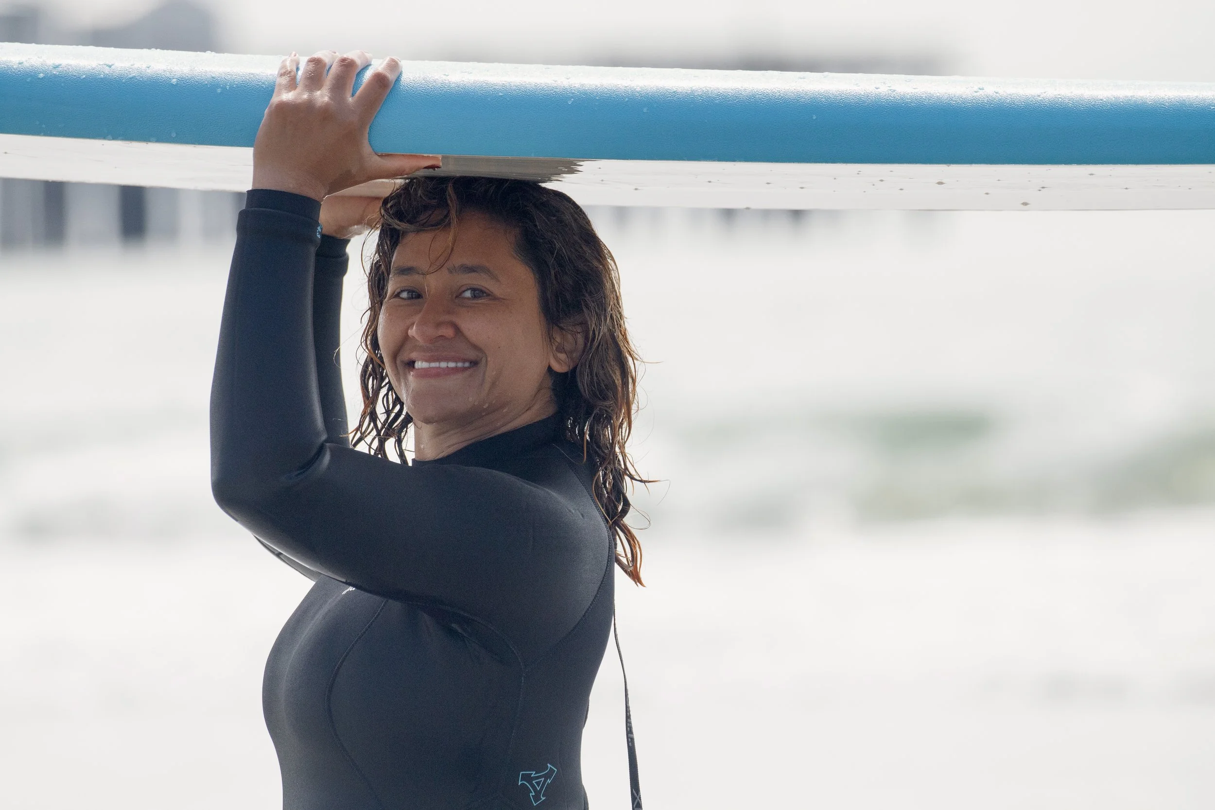 Samantha Juan smiling in a wetsuit while carrying a surfboard during an MIIT activity.
