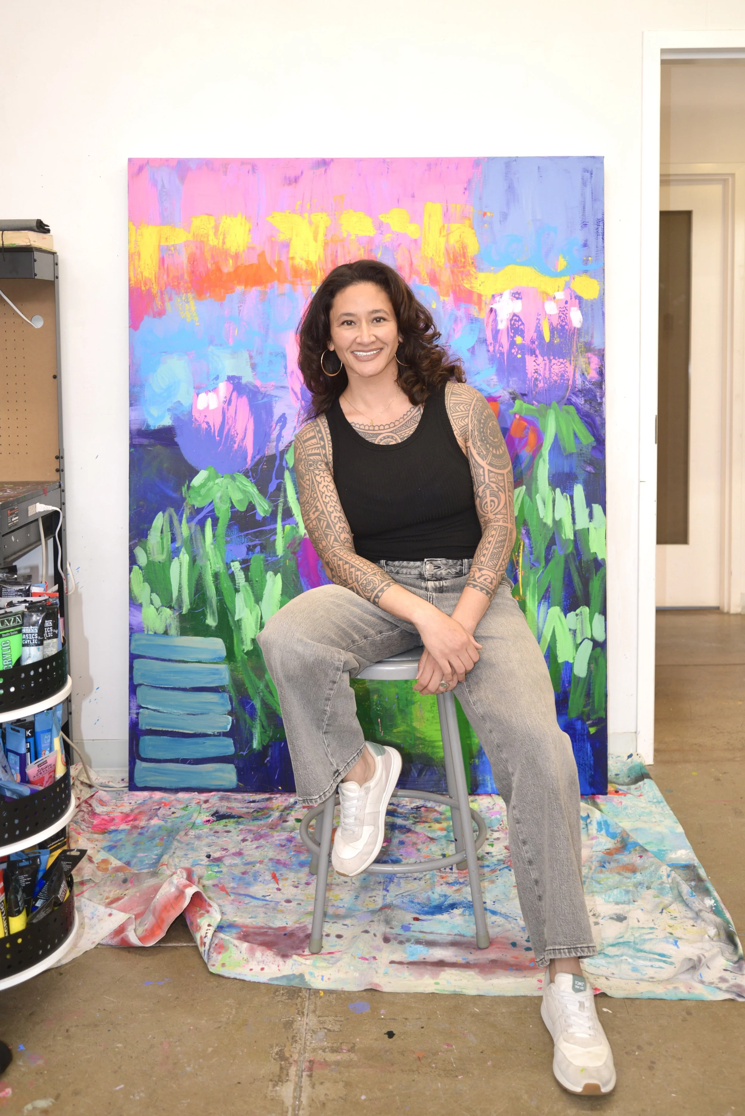 Samantha Juan seated in her art studio surrounded by colorful abstract paintings.