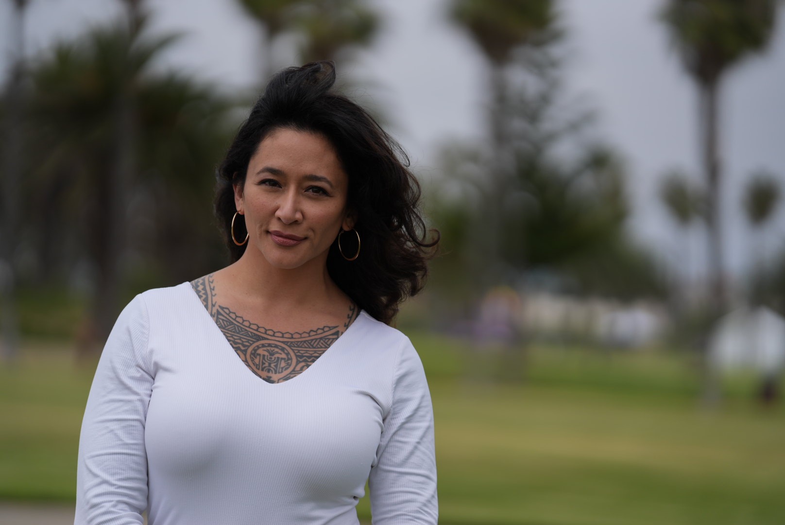 Samantha Juan wearing a white top while standing outdoors in a park with palm trees.