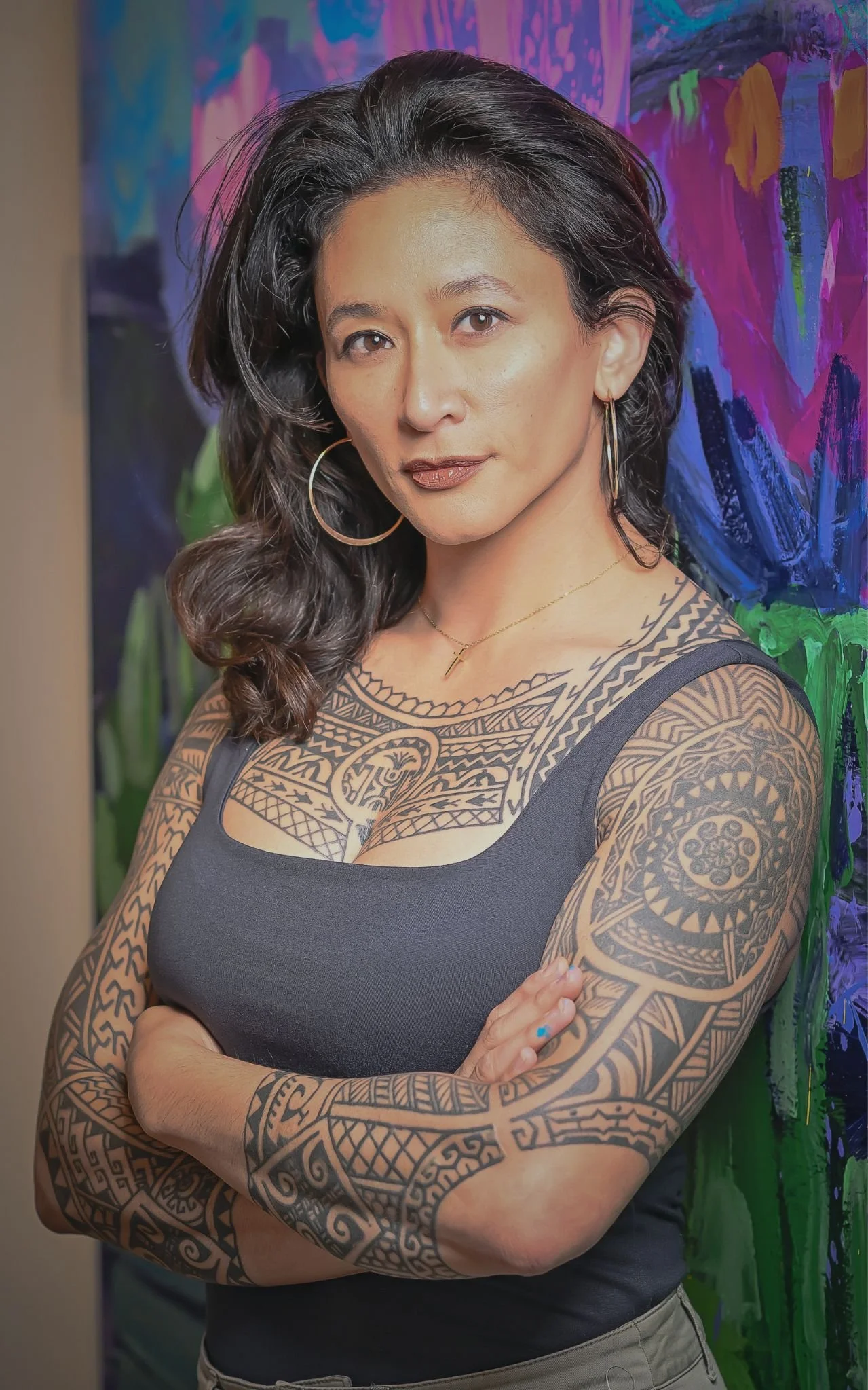 Sam Juan standing with her arms crossed in front of a colorful abstract painting.