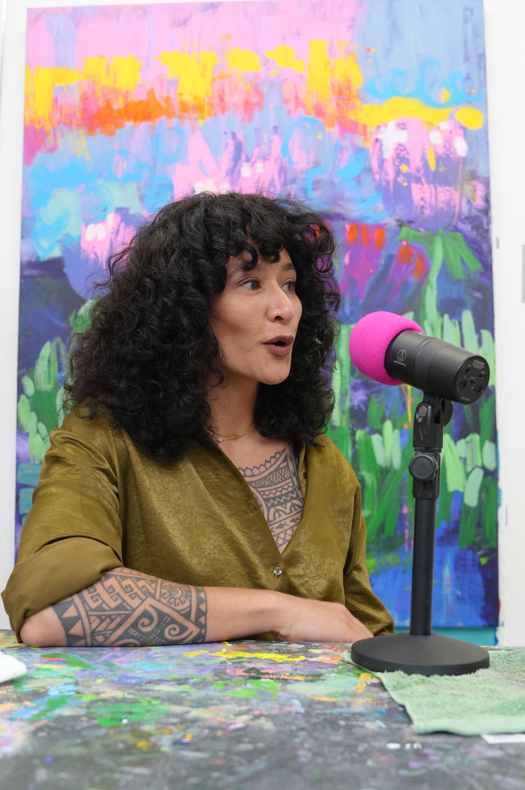 Samantha Juan speaking into a pink microphone during a podcast interview in her art studio.