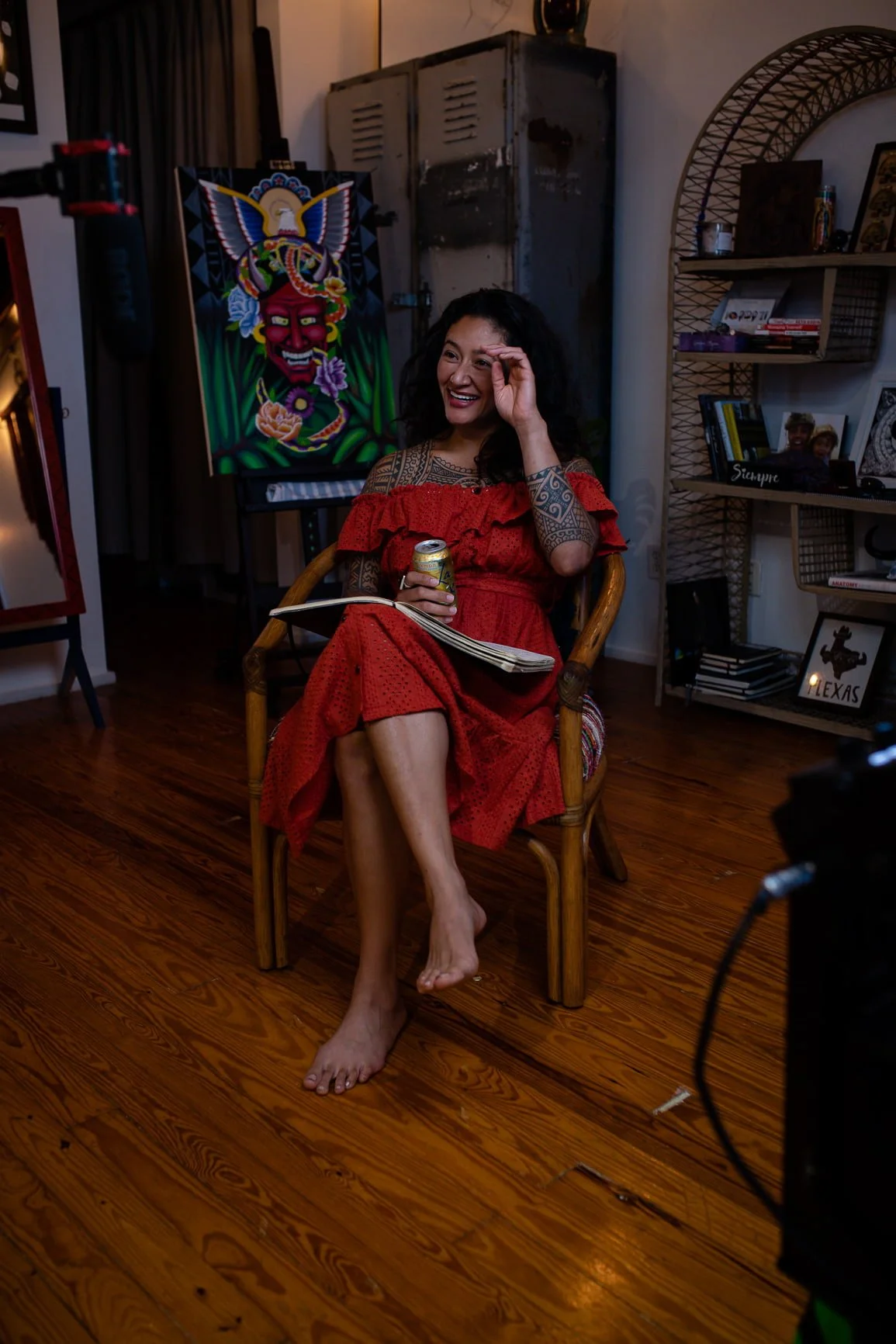 Samantha Juan smiling in a red dress while seated barefoot in an art-filled space during her time in Dallas.