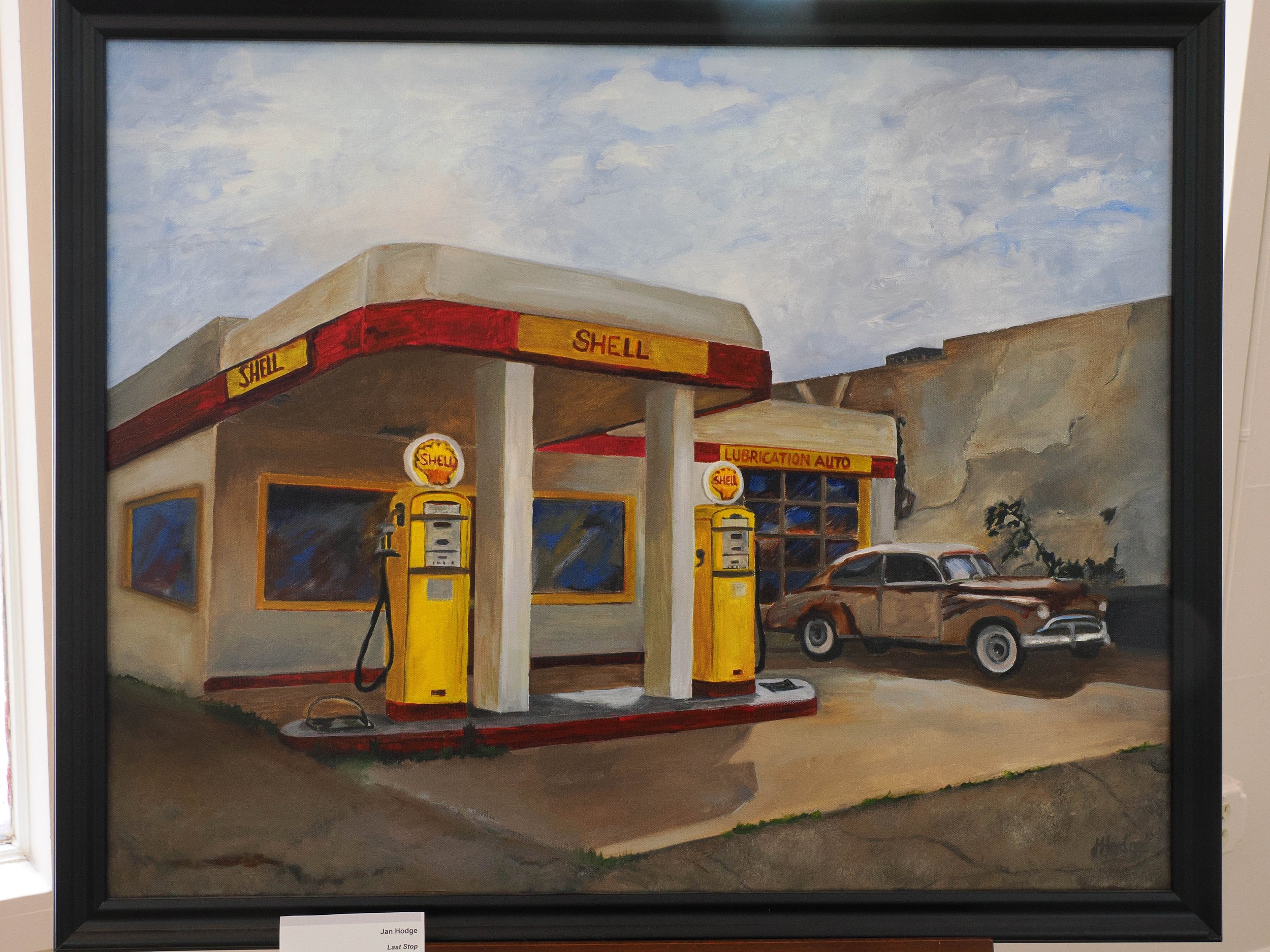 Painting of a Shell gas station with yellow and red signage and two gas pumps in the foreground, a car parked at one of the pumps, and a cloudy sky above.