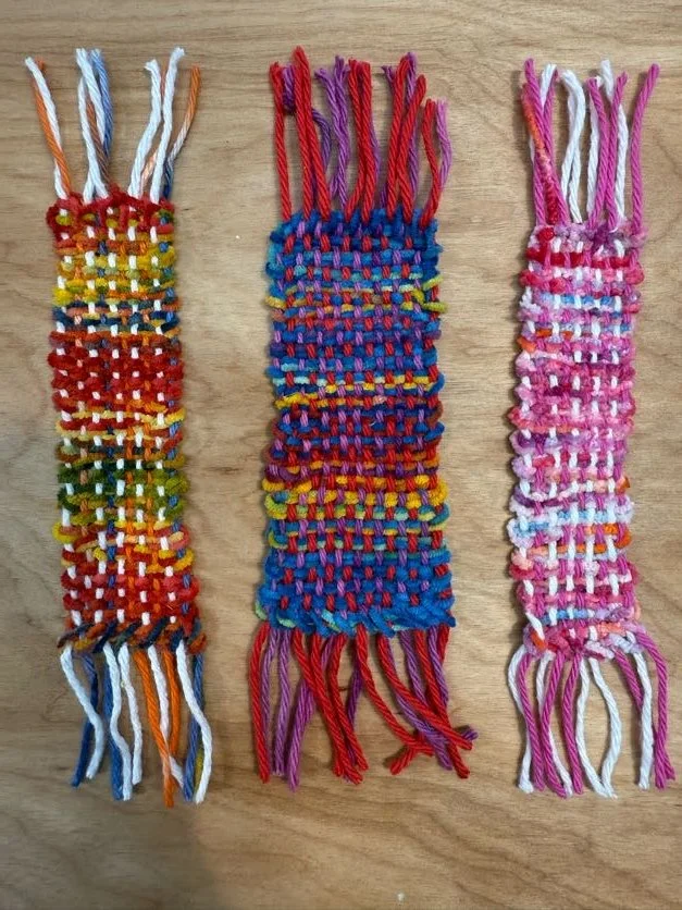 Three handmade friendship bracelets with colorful woven patterns and fringed ends laid out on a wooden surface.