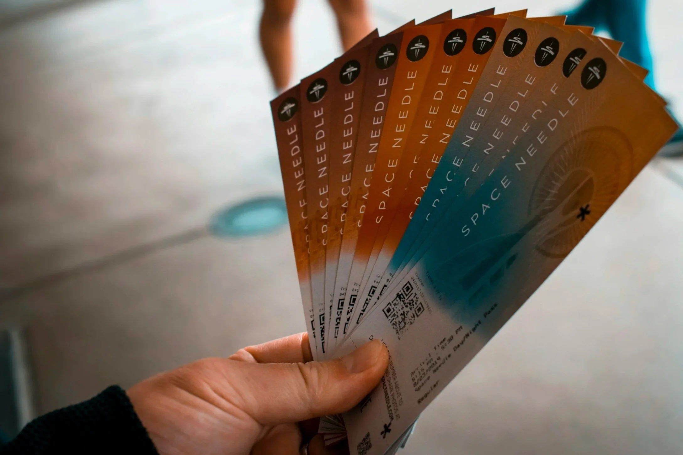 A person holding a fan of airline boarding passes with a background of a person's legs and a blue garment.