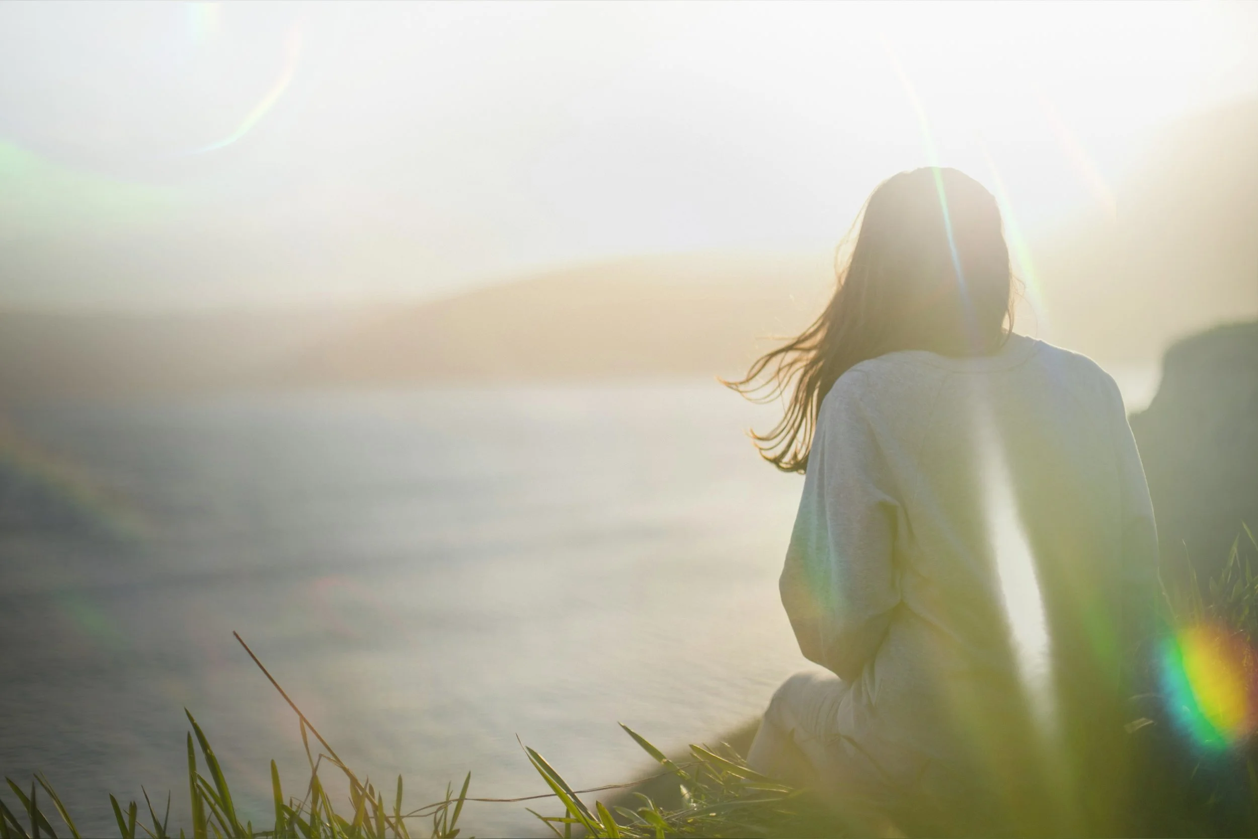 A woman sitting on grass near water during sunset