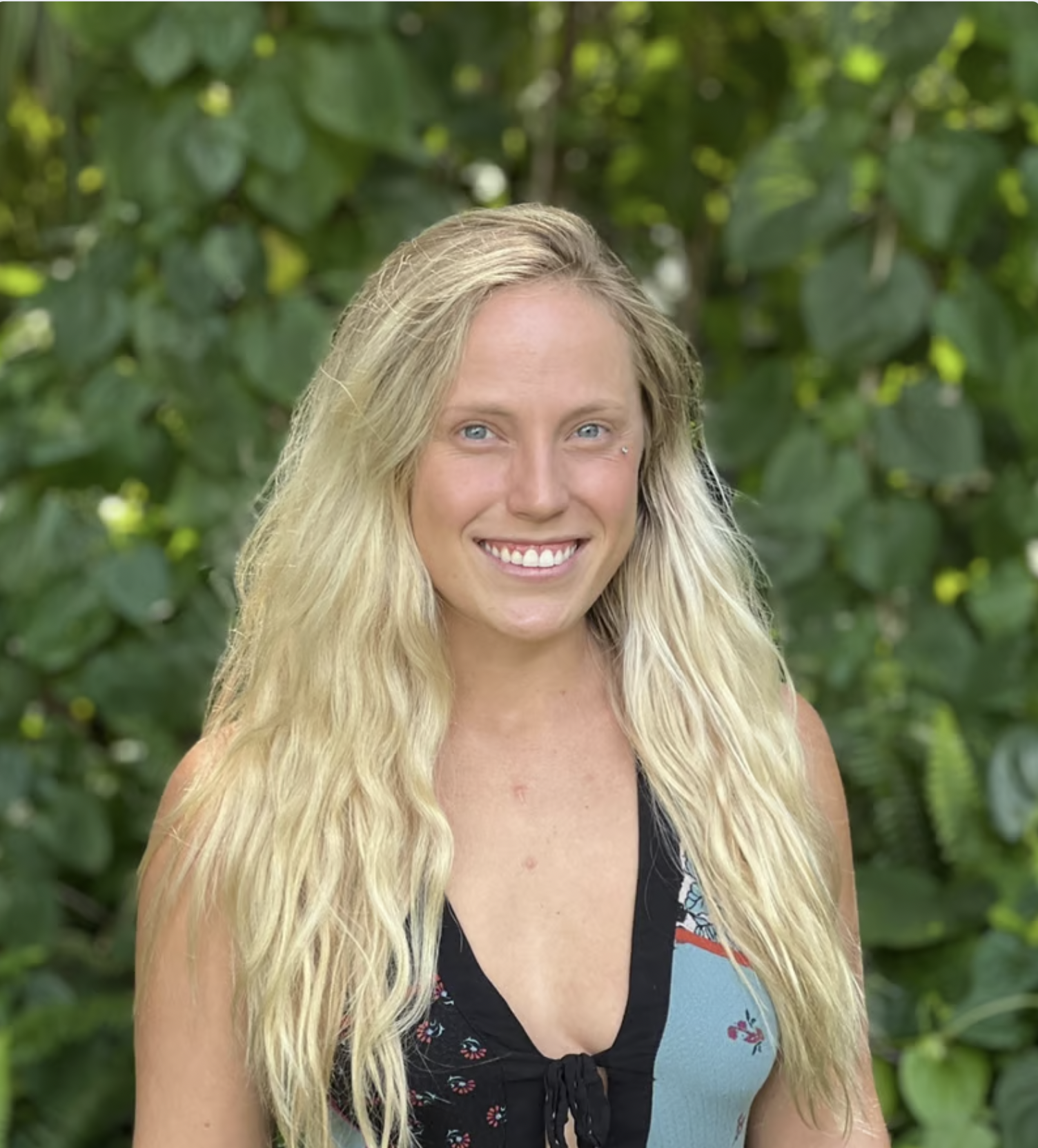 Blonde woman smiling outdoors in front of green foliage