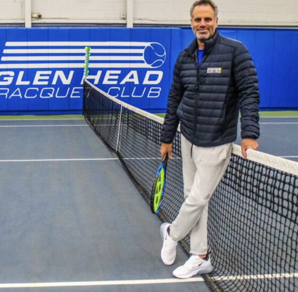A man holding a tennis racket standing on a tennis court next to the net at Glengate Racquet Club.