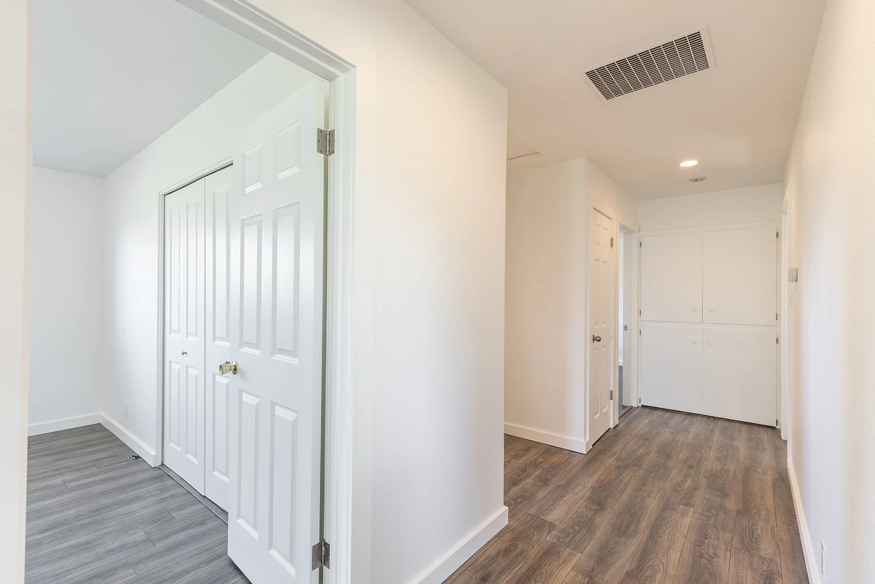 Empty hallway with white walls, wooden flooring, and multiple closed doors.