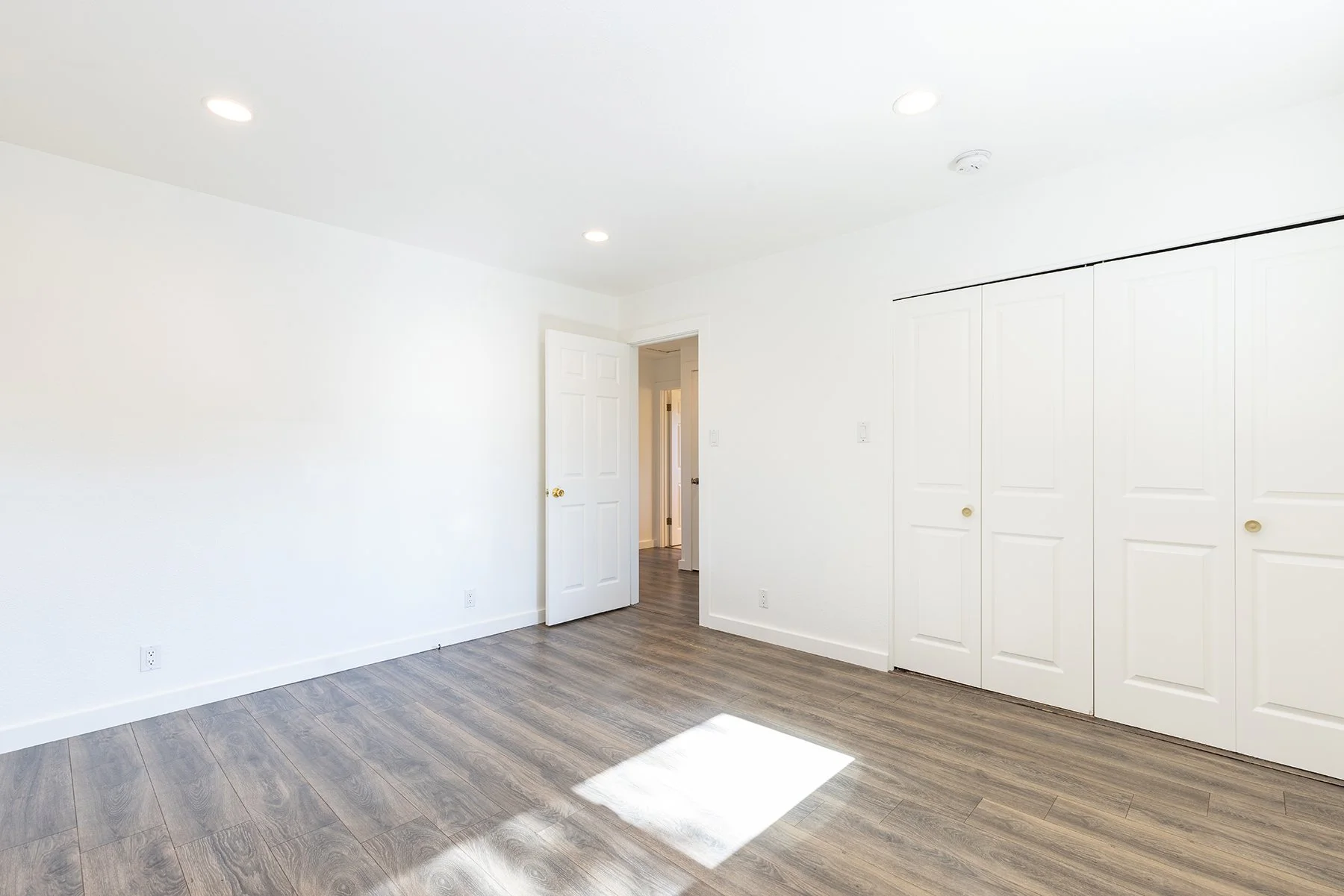 Empty room with white walls, wood flooring, a doorway, and a closet with sliding doors.