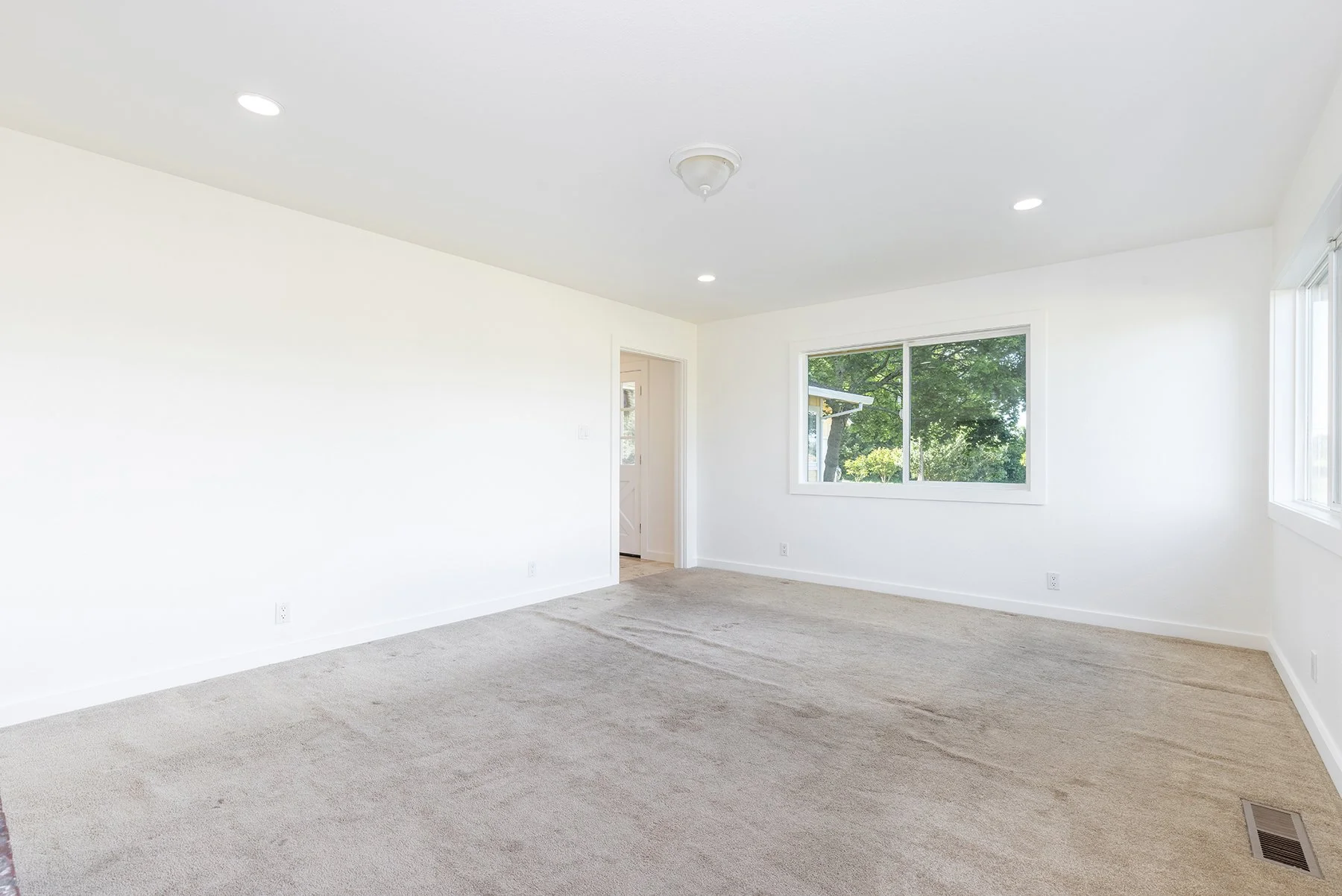 Empty white room with large windows, beige carpet, and ceiling lights.