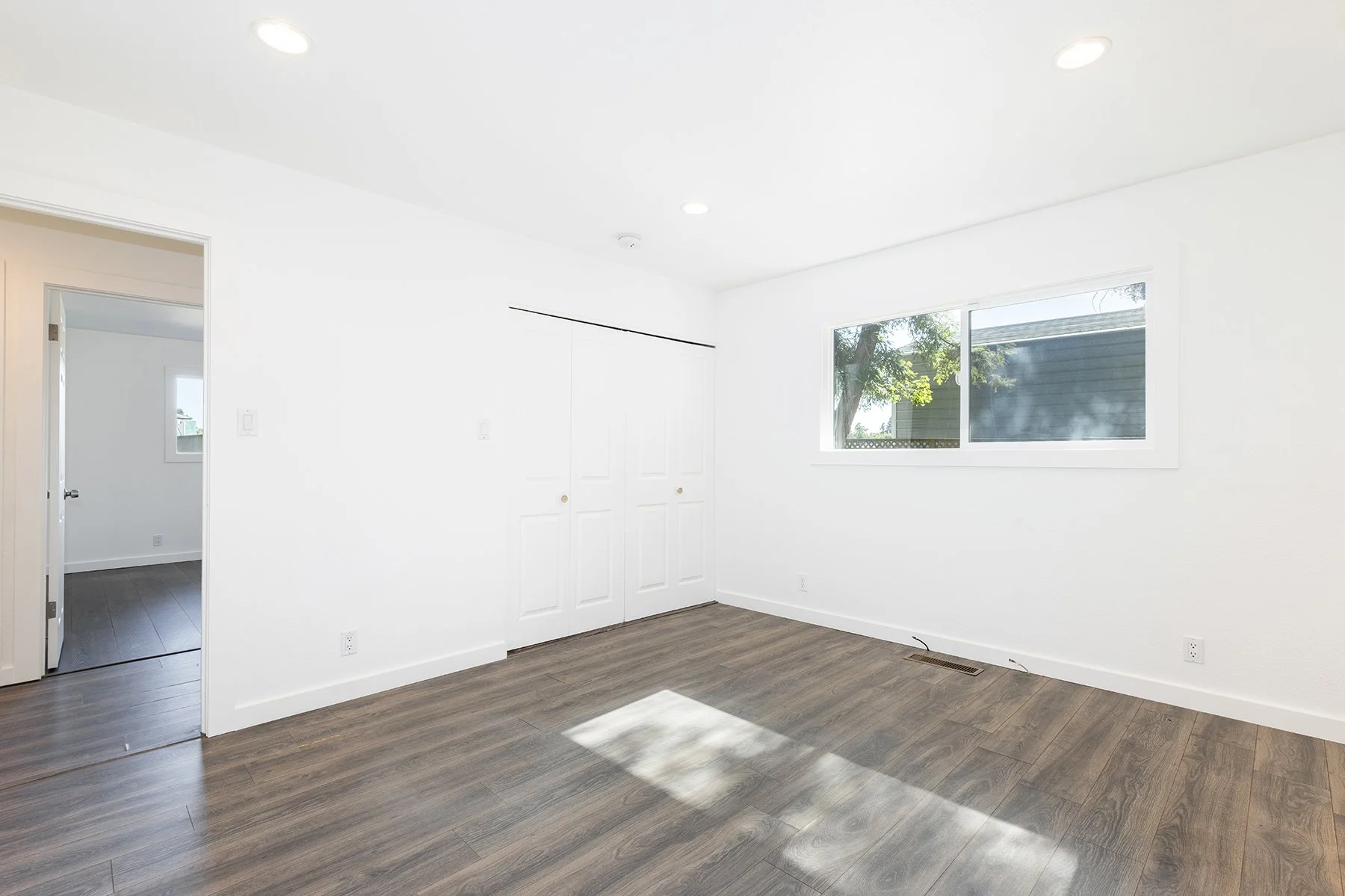Empty room with white walls, large window, hardwood flooring, and closet with sliding doors.