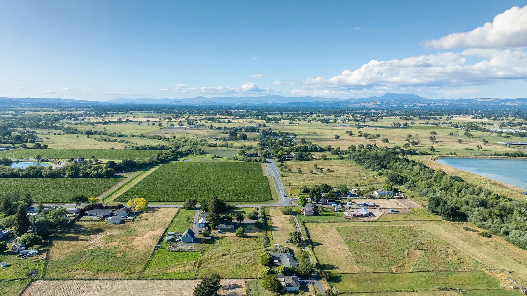 Aerial view of a rural landscape with fields, farmhouses, and ponds under a partly cloudy sky.