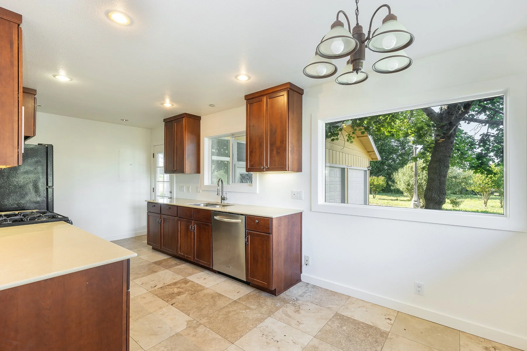Kitchen with wooden cabinets, a window showing a yard with trees, and a chandelier overhead.