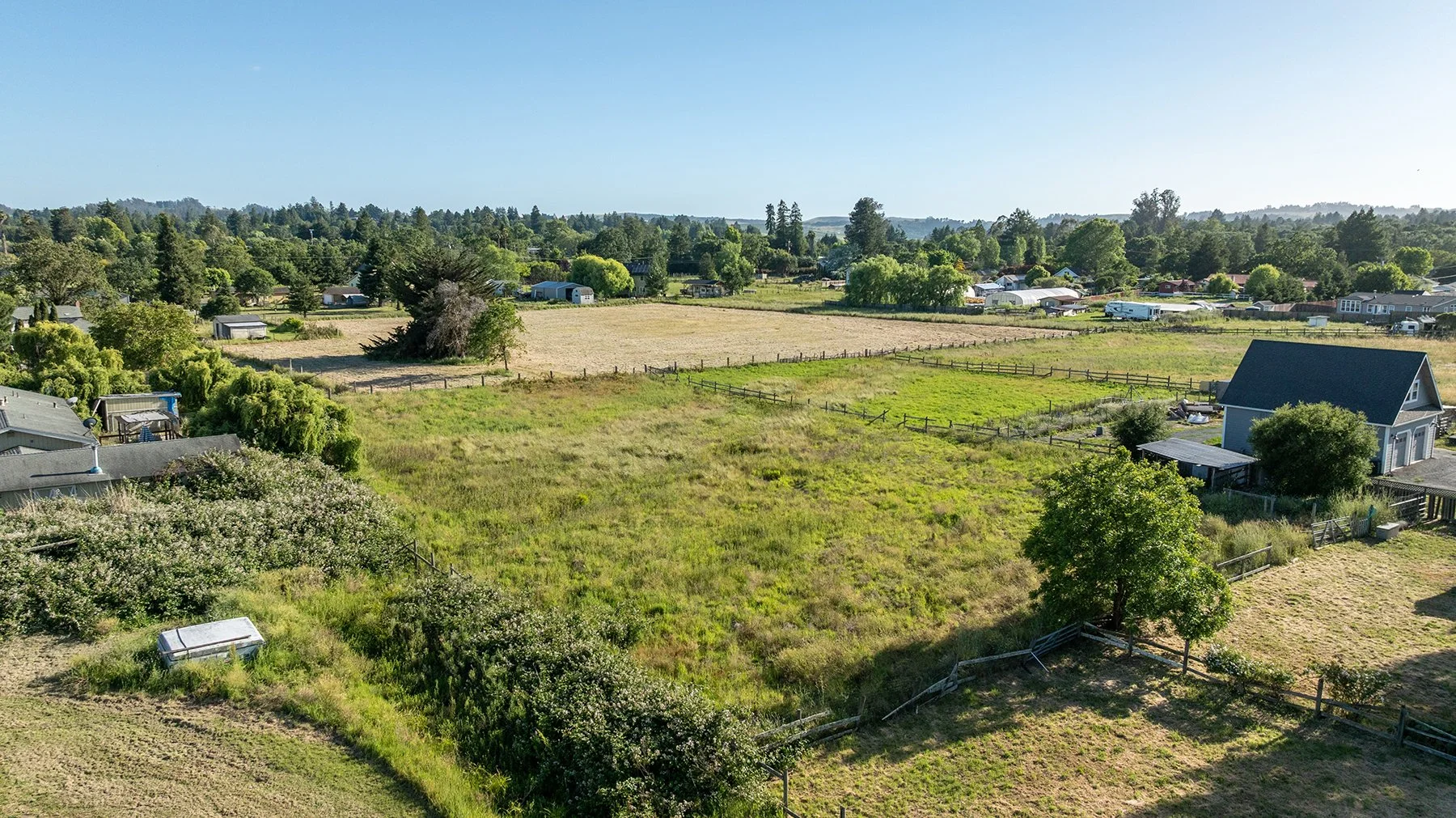 A rural landscape with green fields, trees, and scattered houses under a clear blue sky.
