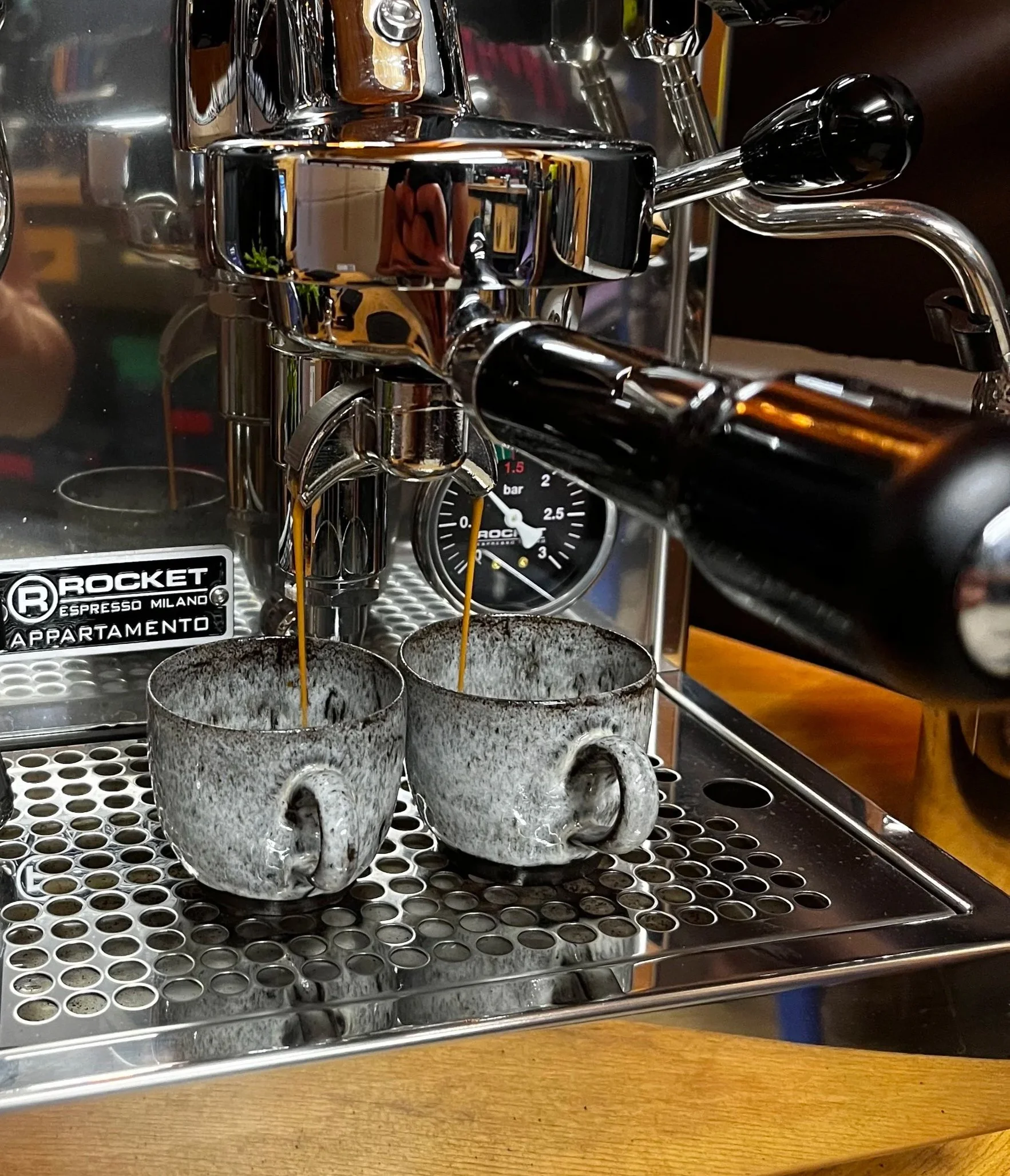 Eine Espressomaschine bei der Zubereitung von Kaffee, zwei Tassen mit frisch gebrühtem Kaffee unter Ausläufen, das Ganze steht auf einem Metalltablett