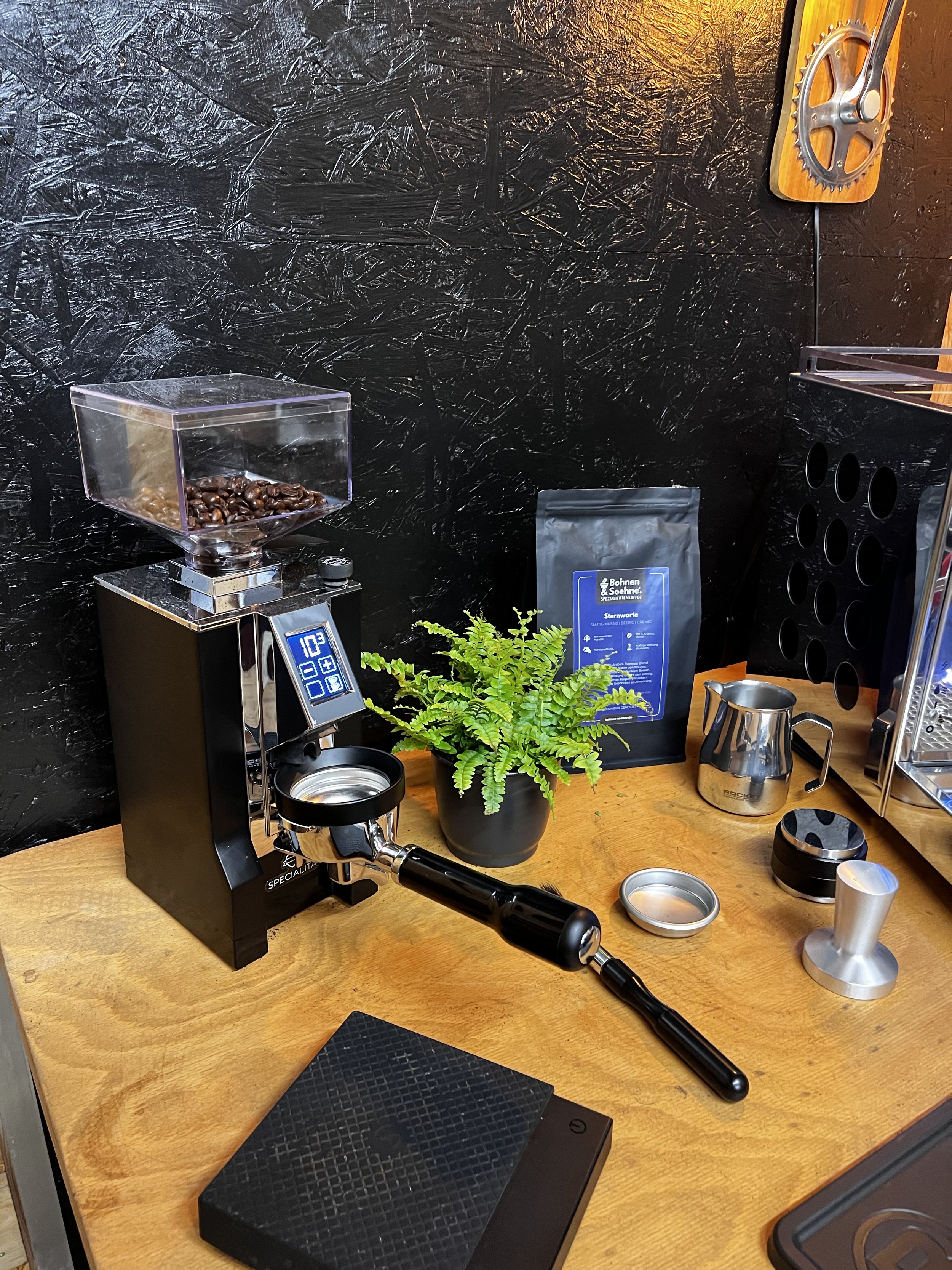 Eine Kaffeemaschine, Kaffeebohnen, eine Pflanze und Arbeitsutensilien auf einem Holztisch.