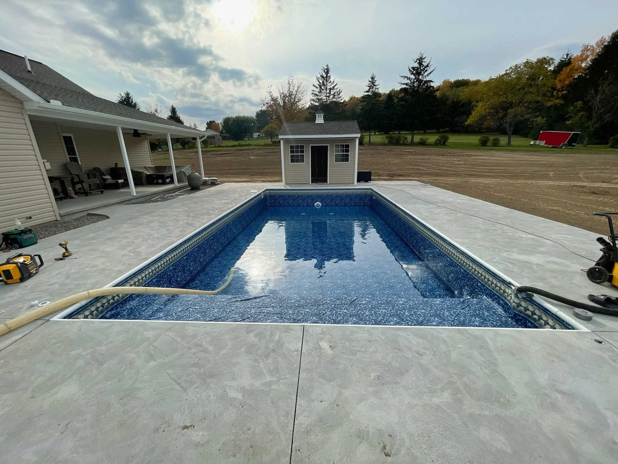 In-ground swimming pool under construction beside a covered patio and backyard entertainment area.