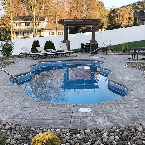 Freeform in-ground swimming pool with stamped concrete patio and pergola seating area.