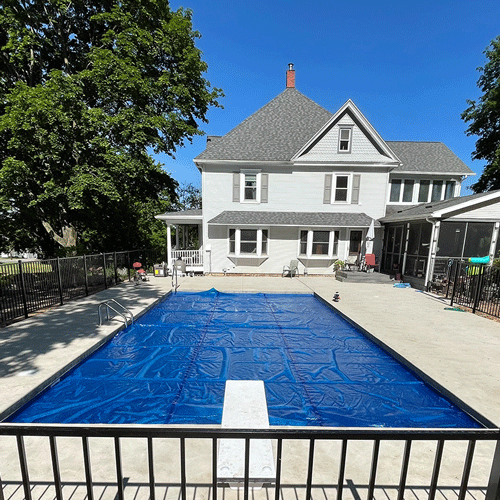 Custom backyard swimming pool with curved design, concrete decking, and fenced yard.