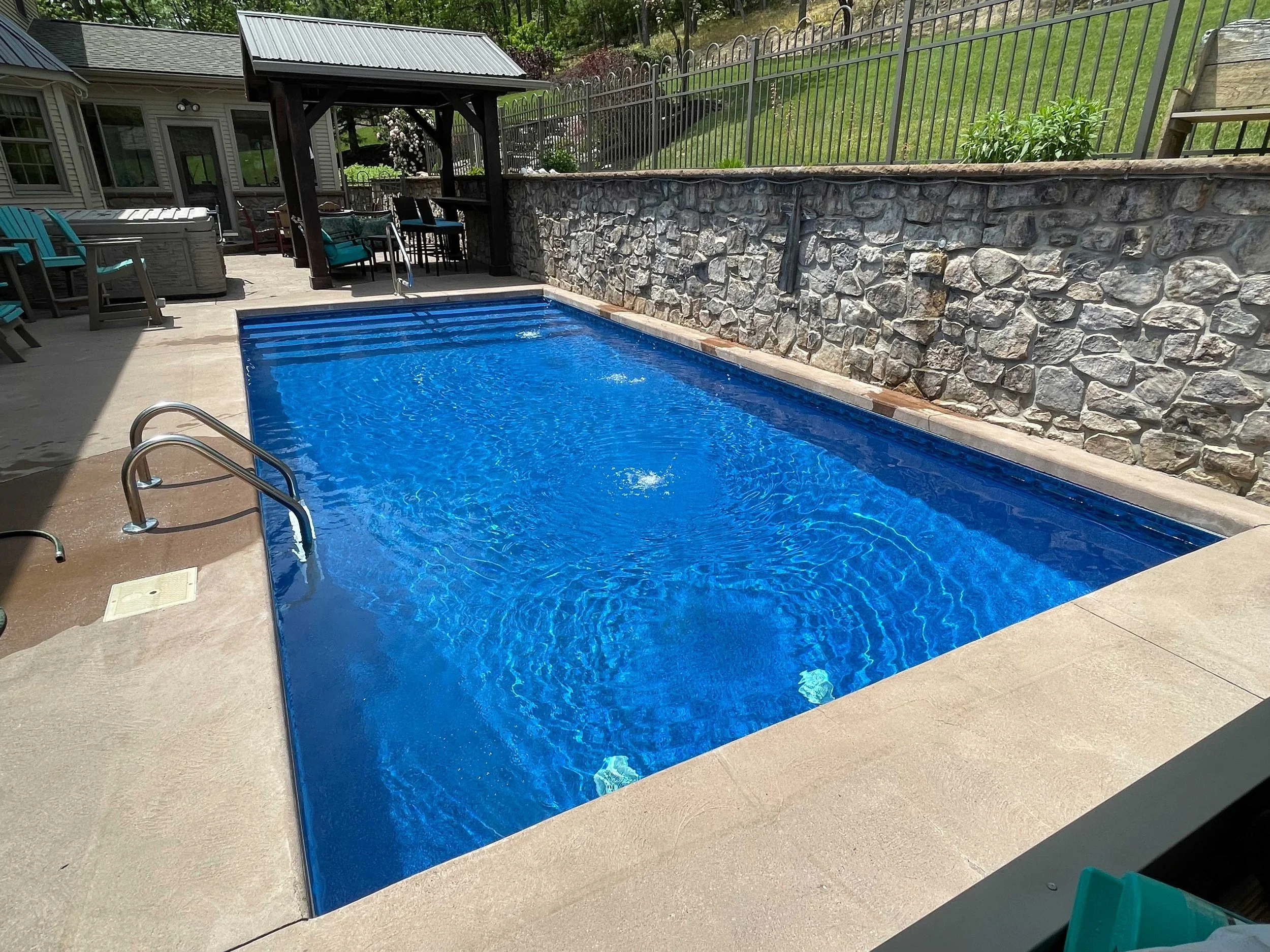 Rectangular in-ground swimming pool with stone retaining wall and covered outdoor seating area