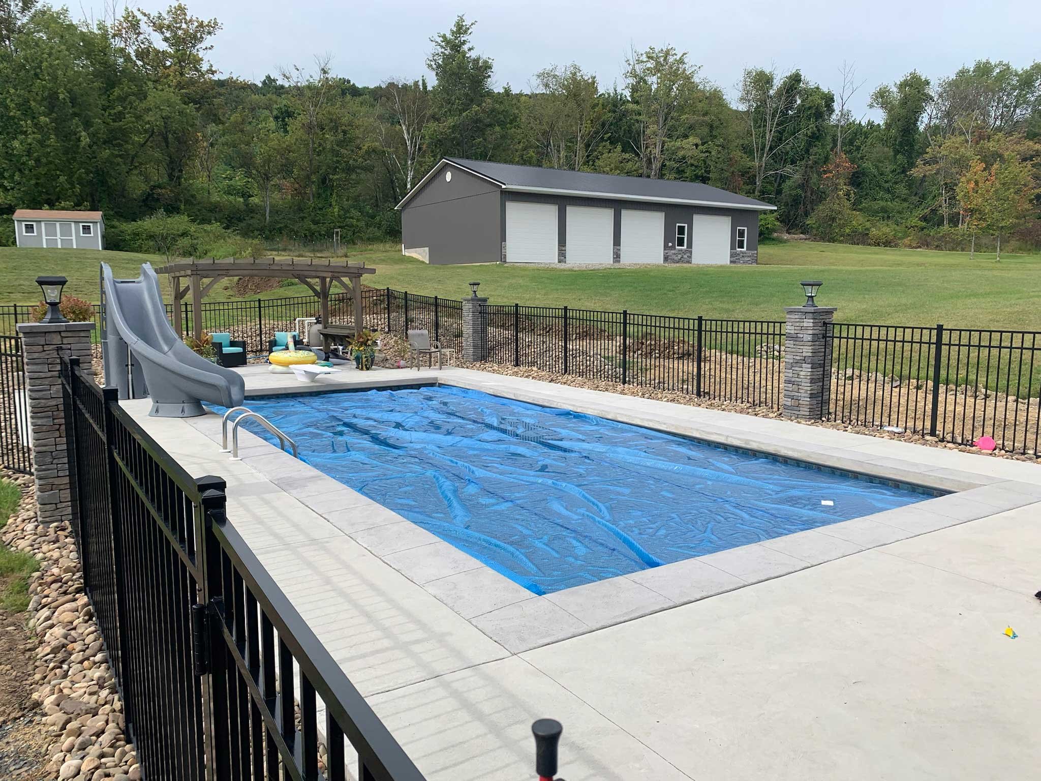Rectangular swimming pool with slide, pergola seating area, and safety cover