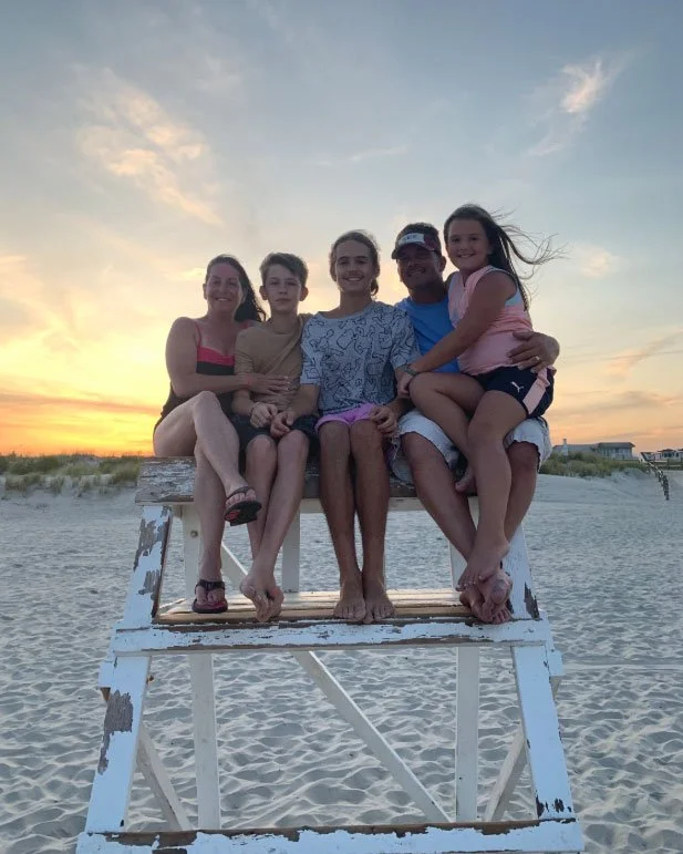 Eric Brown, owner of Man Made Pools, sitting with his family on a lifeguard stand at the beach during sunset.