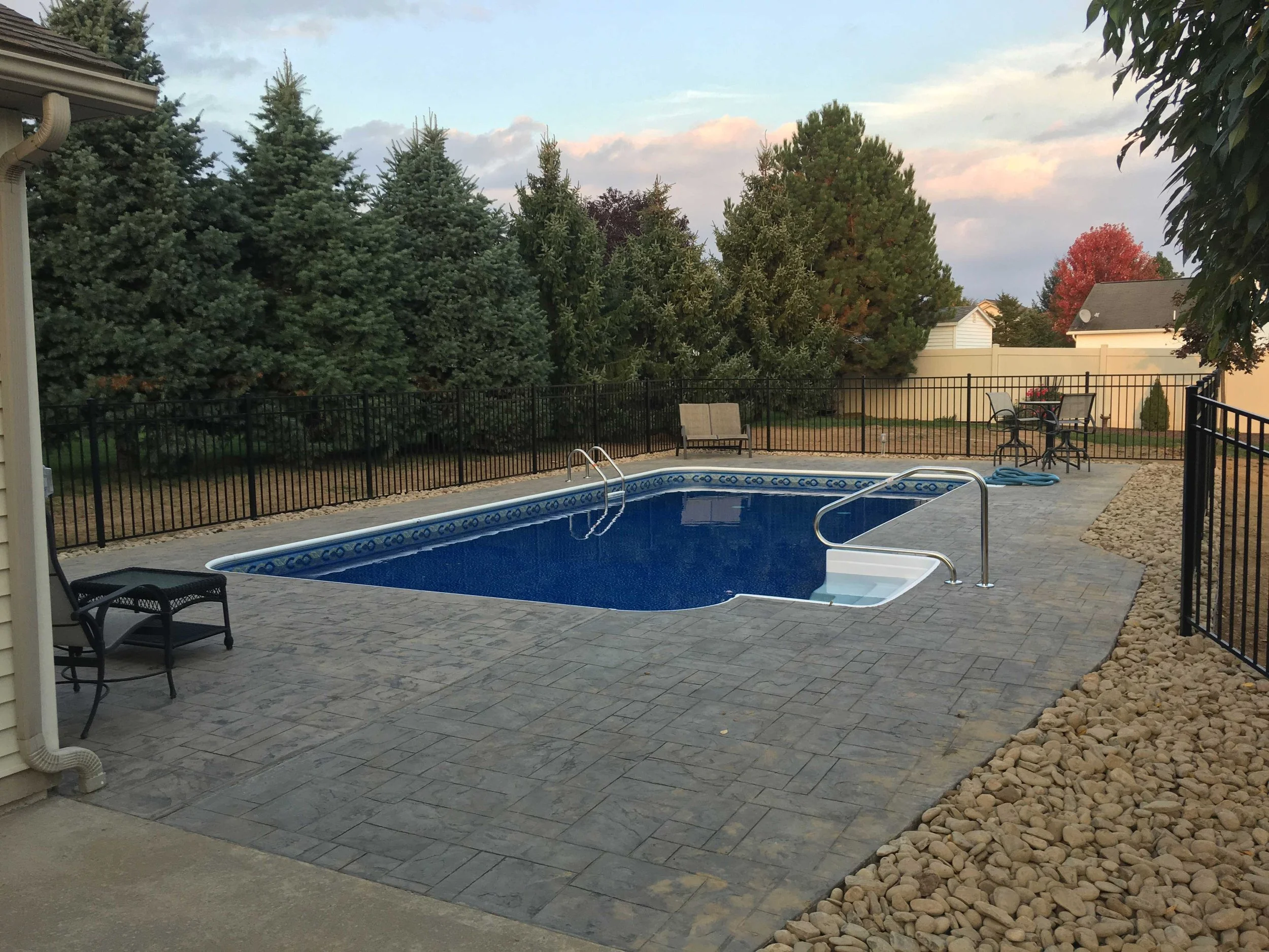 Custom in-ground swimming pool with stamped concrete patio, black fencing, and landscaped backyard