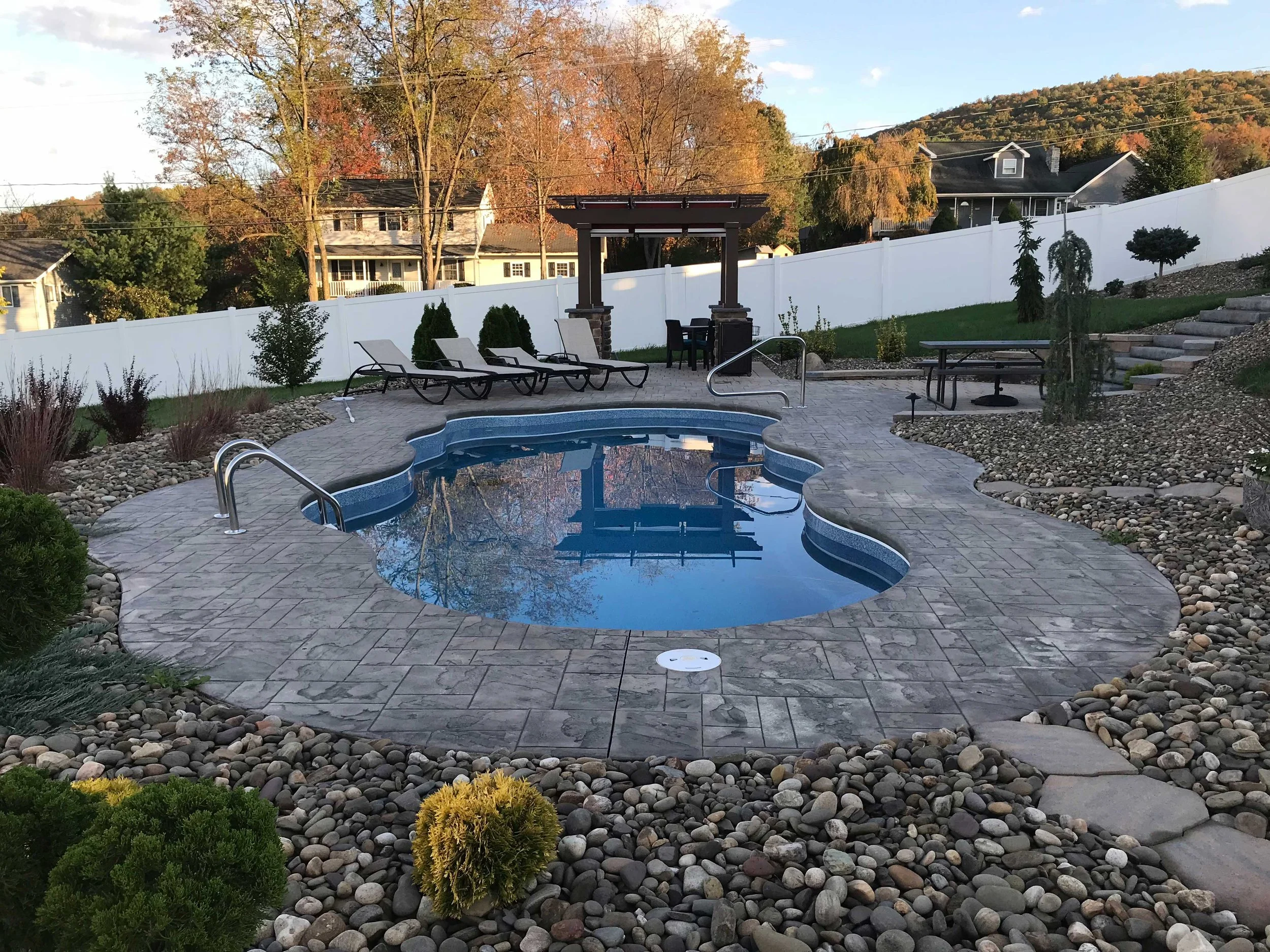 Freeform in-ground swimming pool with stamped concrete patio, pergola, and landscaped backyard