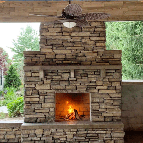 Stone outdoor fireplace and covered patio area completed as part of a custom backyard living space.