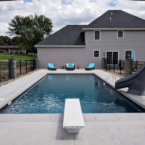 Custom rectangular in-ground pool with diving board, slide, and surrounding concrete deck.