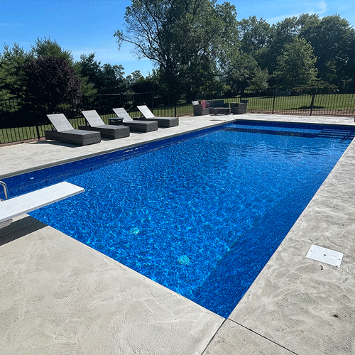 Residential in-ground swimming pool with crystal-clear water, diving board, and poolside lounge chairs.
