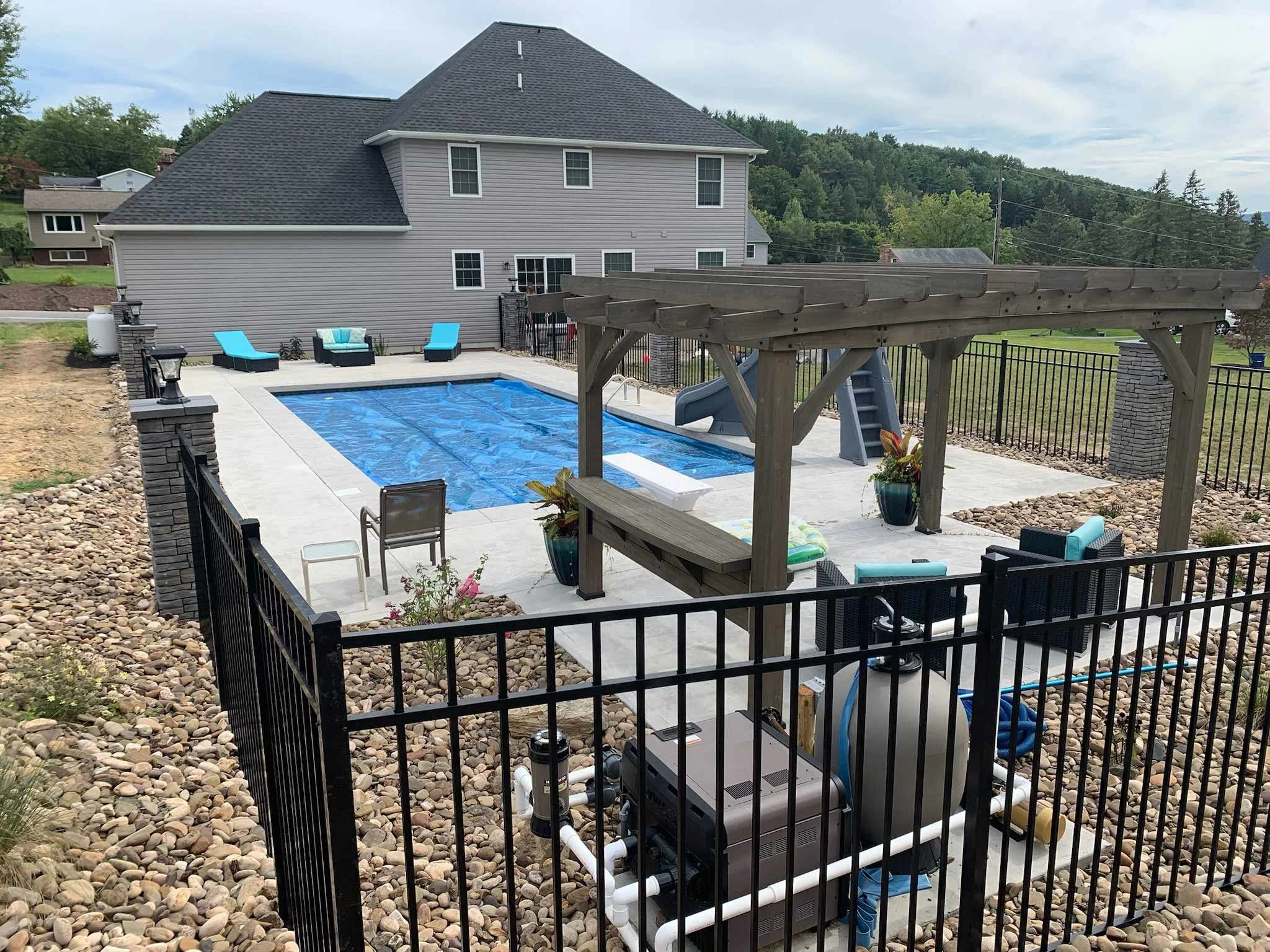 Backyard pool featuring a safety cover, pergola, concrete patio, and black aluminum fencing.
